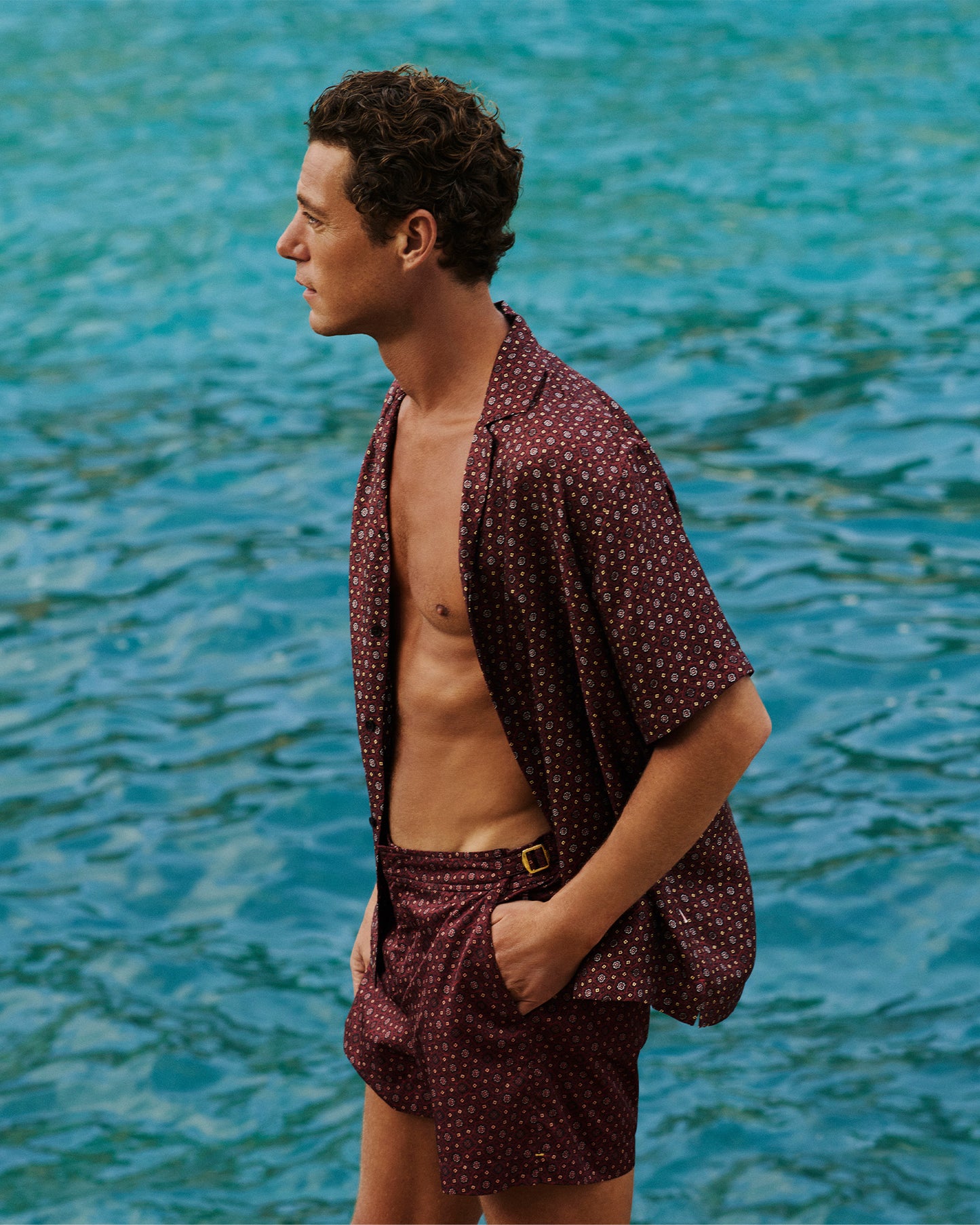 Man wearing printed open shirt with matching swim shorts against backdrop of the ocean