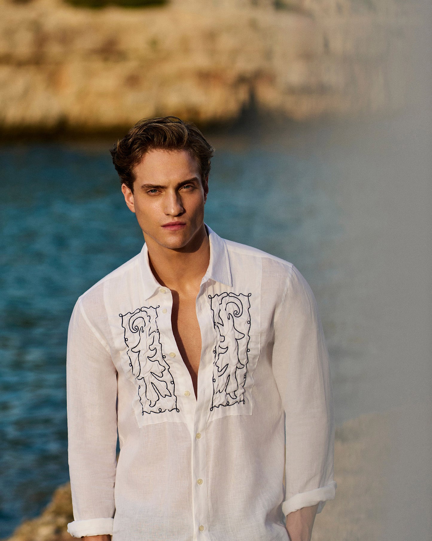 Man wearing a white embroidered shirt by a body of water
