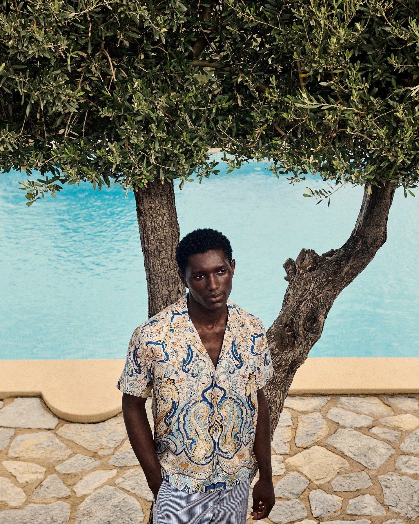 Man standing by a poolside with a tree in the background