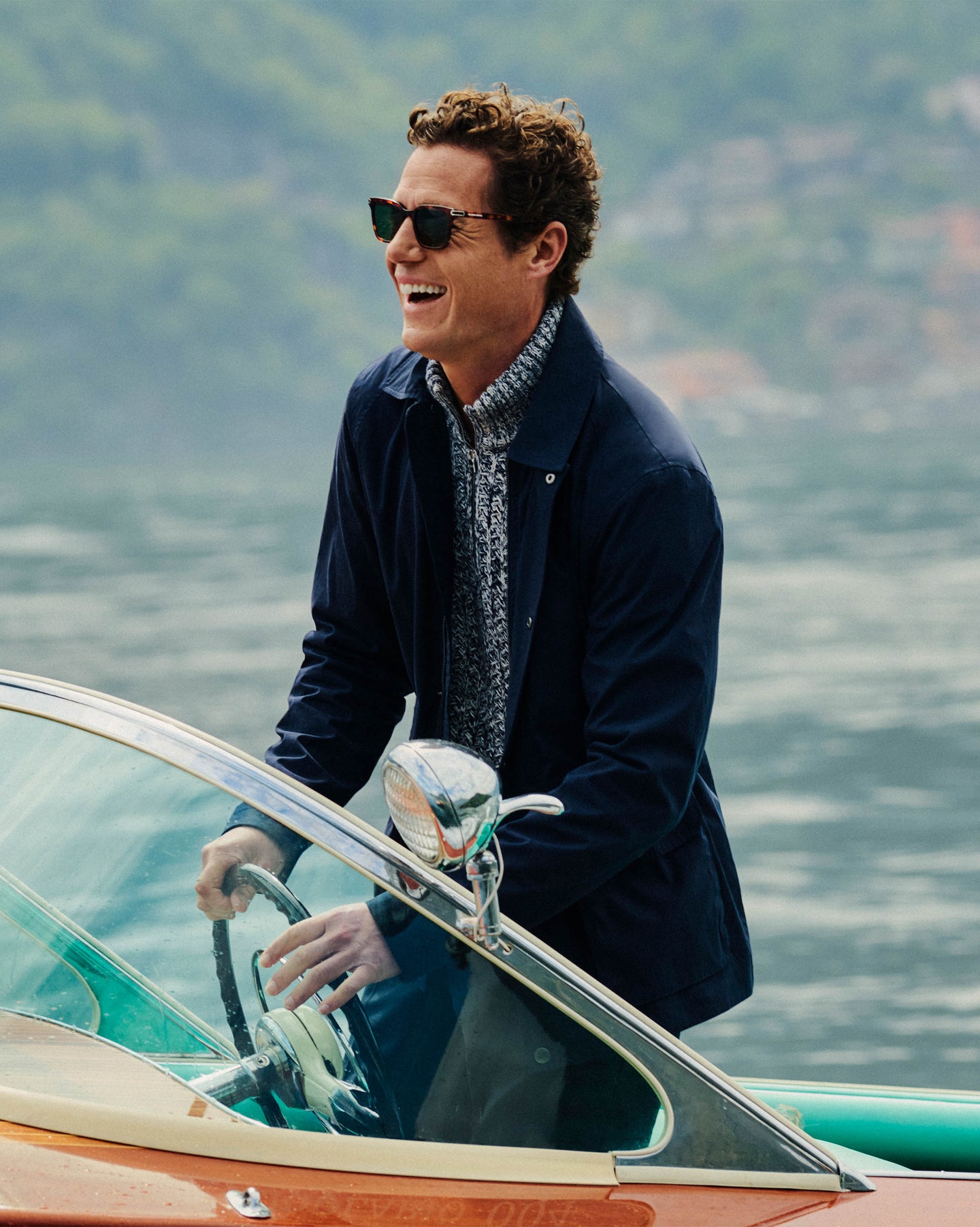 Man on a boat wearing sunglasses and a dark coat with a blurred natural background