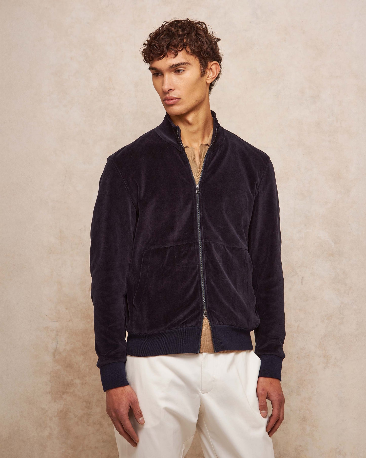 Man wearing a navy blue jacket and white pants against a beige background