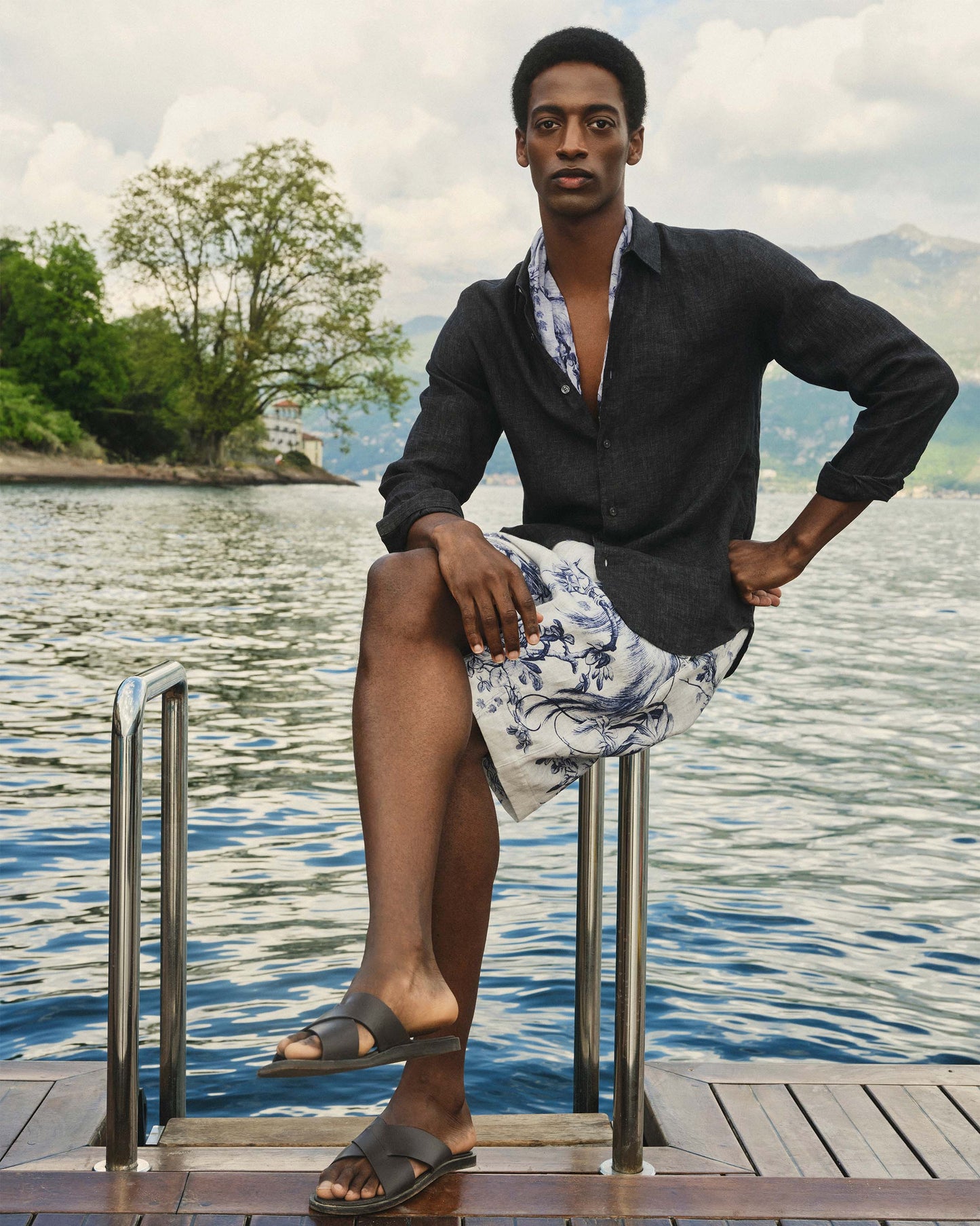 Man sitting on a dock by a lake with mountains in the background
