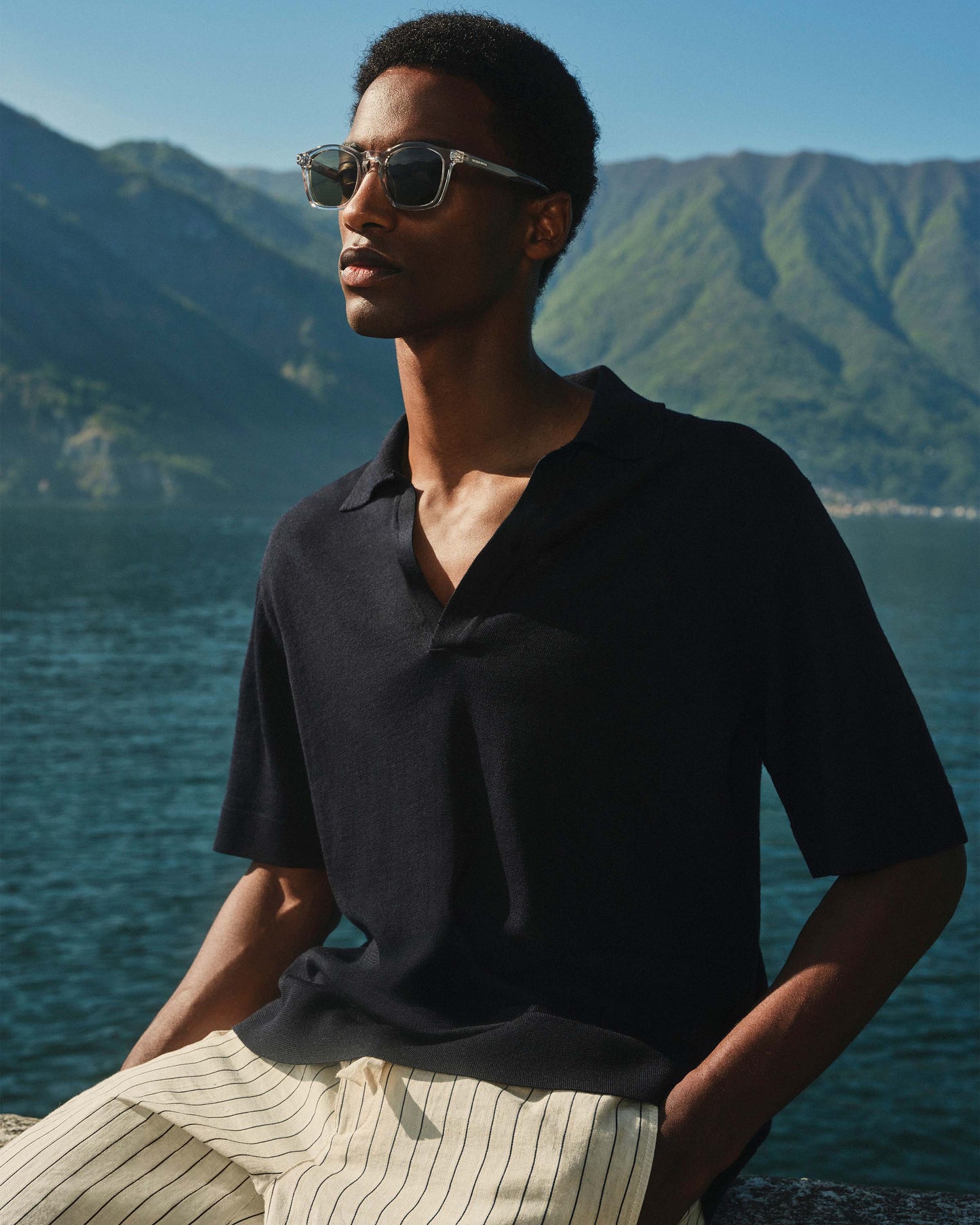 Man wearing sunglasses and a black shirt with mountains and water in the background