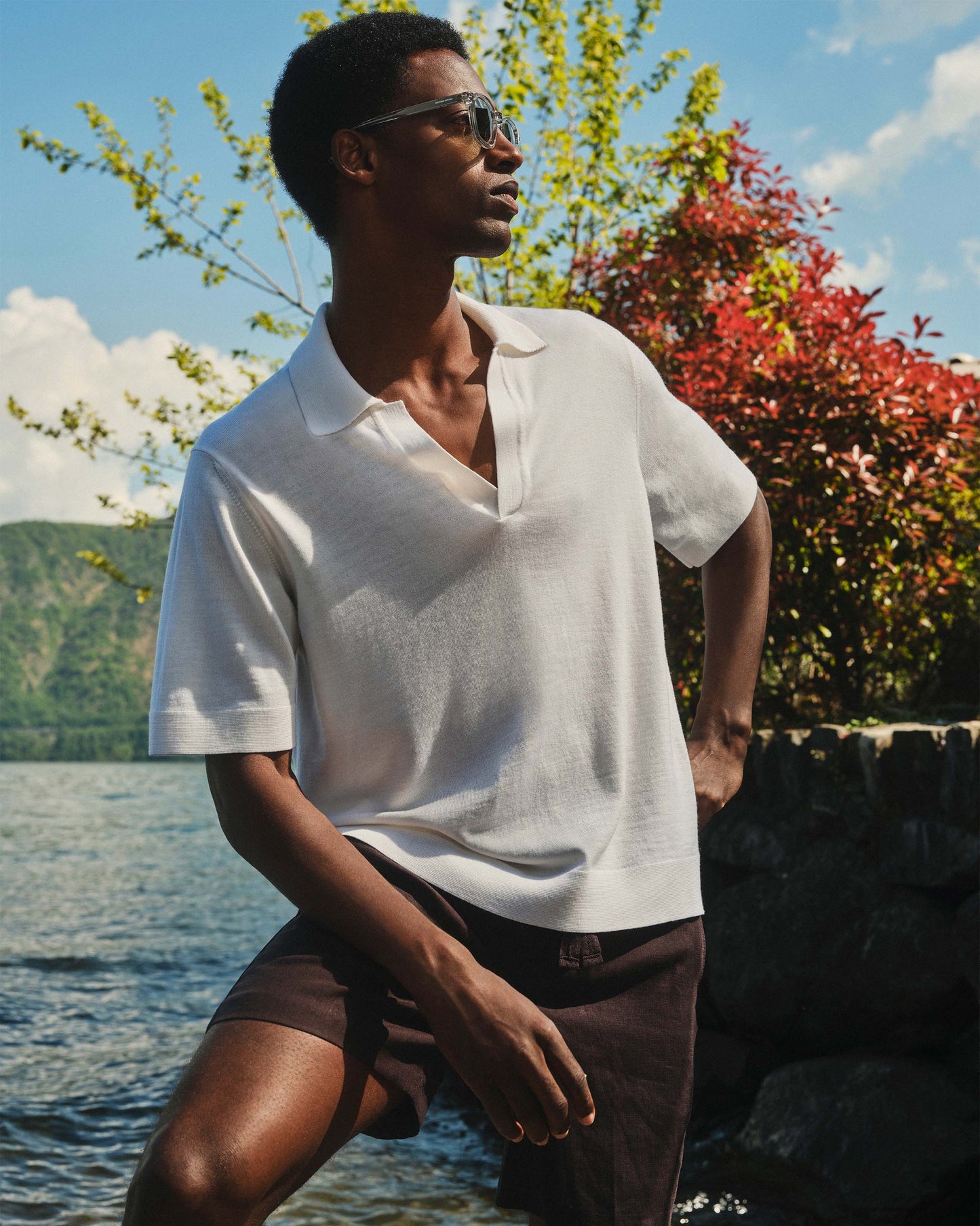 Man wearing a white polo shirt and sunglasses by a lake with trees in the background