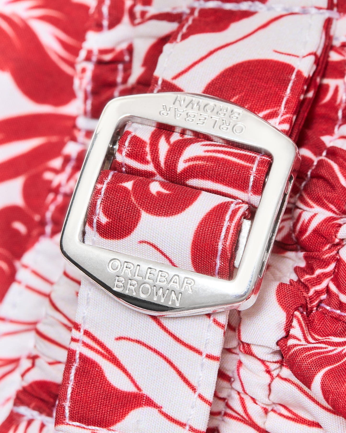 Close-up of an Orlebar Brown belt buckle on a floral-patterned short