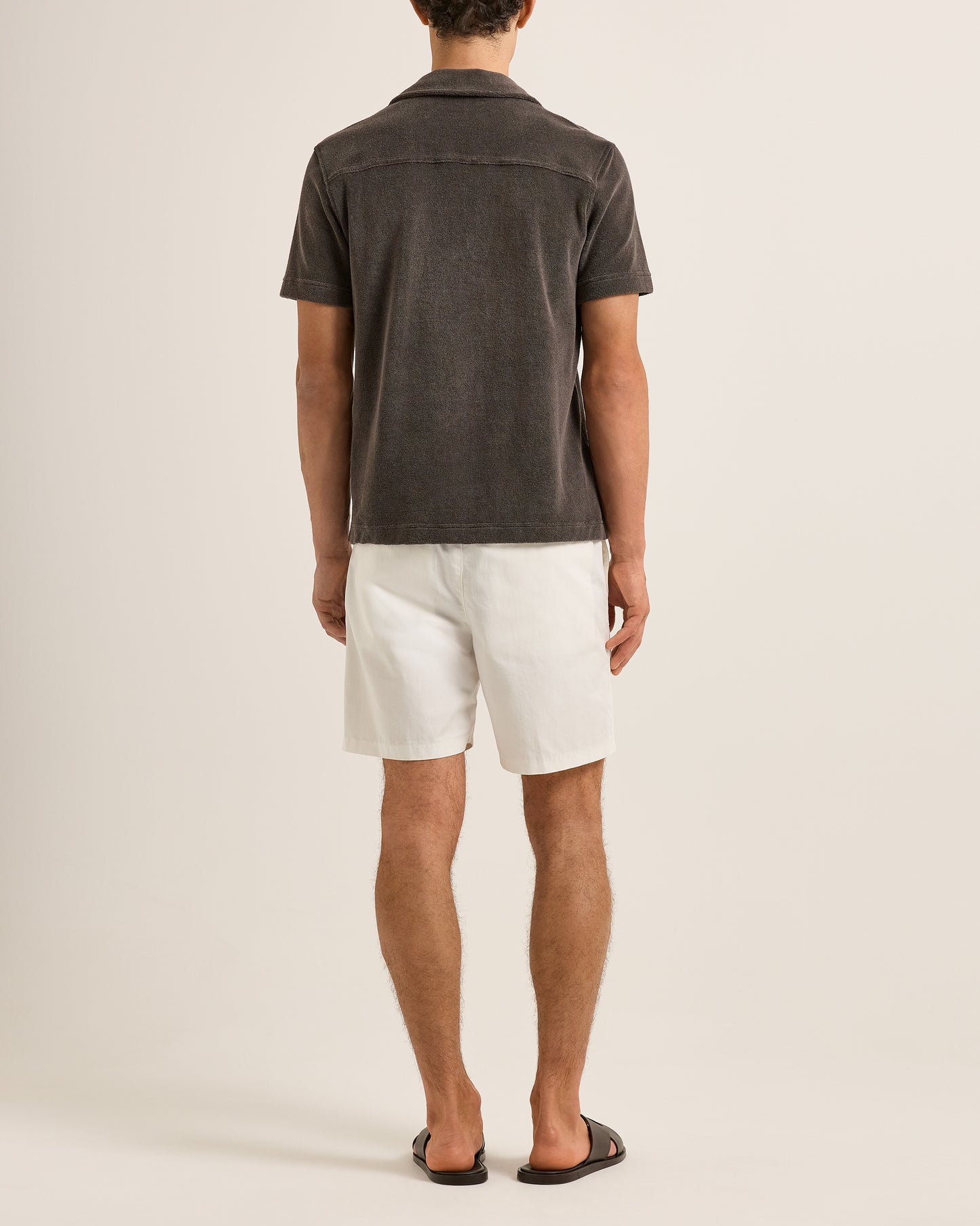Person wearing a dark gray shirt and white shorts on a plain background