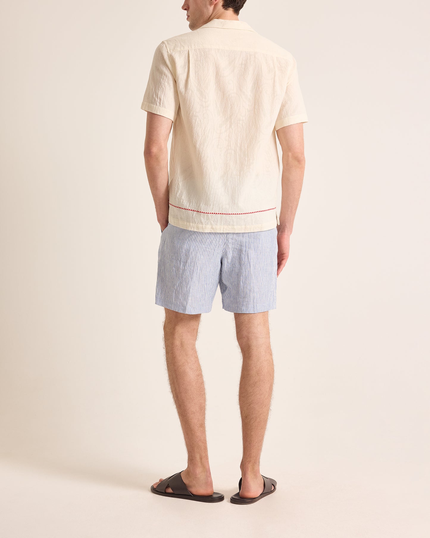 Man wearing a light-colored shirt and blue shorts on a plain background