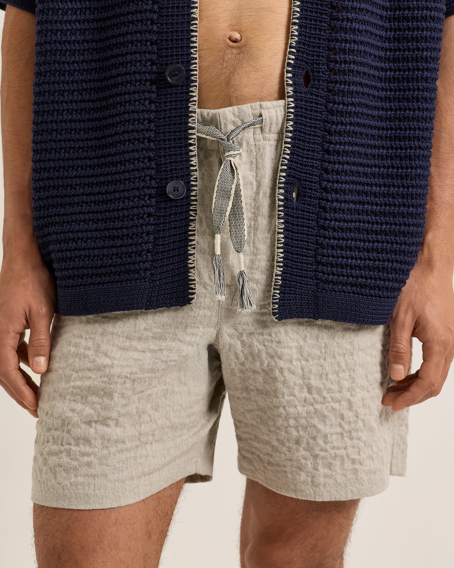 Person wearing a navy textured shirt over a light gray shirt and beige shorts on a neutral background