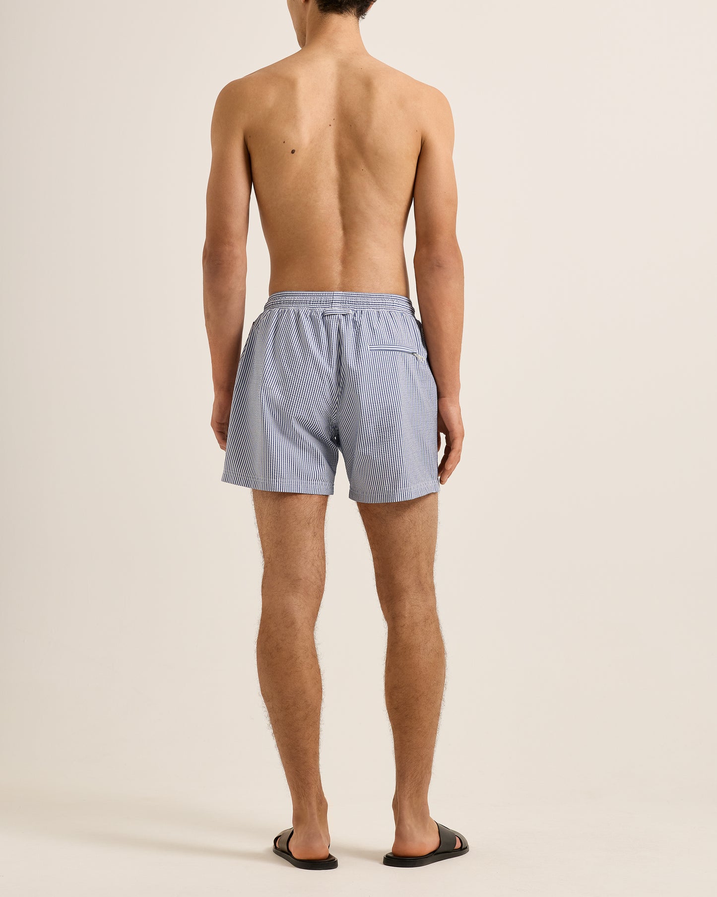 Man wearing light blue swim shorts on a beige background