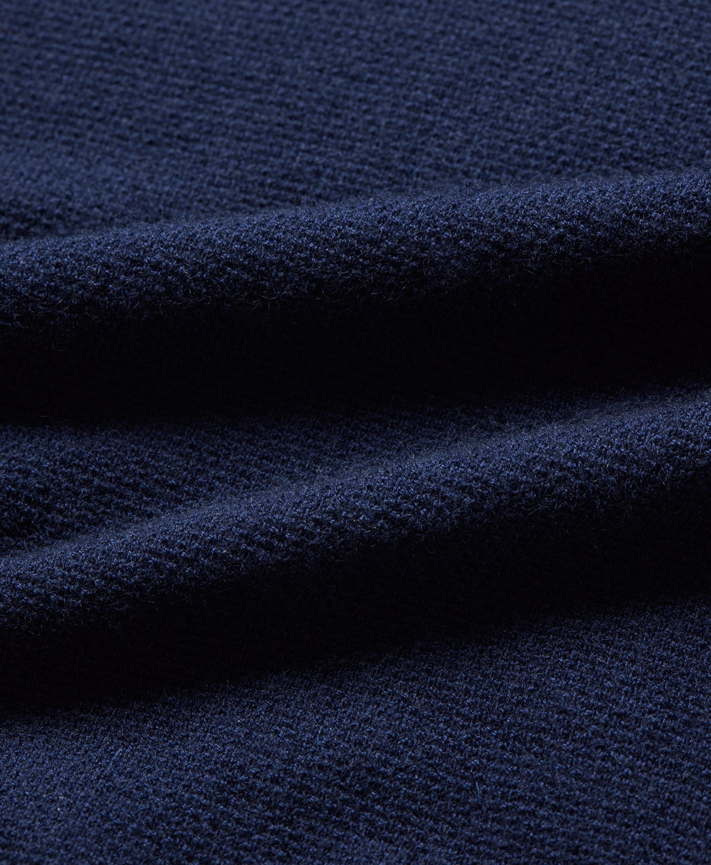 A close-up of dark navy blue knit fabric with soft folds showing the textured weave.