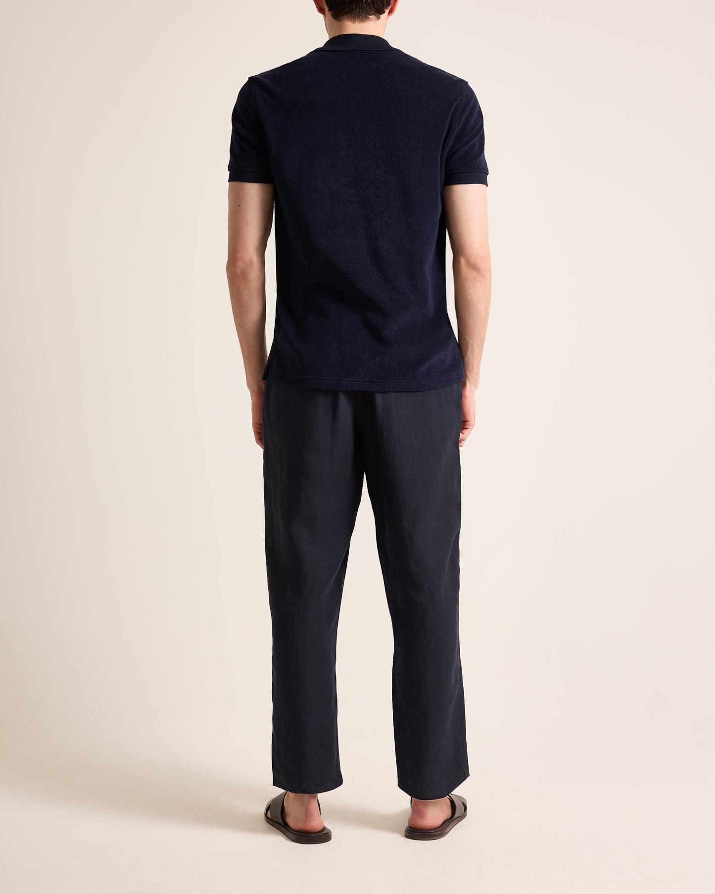 Person wearing navy towelling polo shirt and navy linen trousers on a plain background