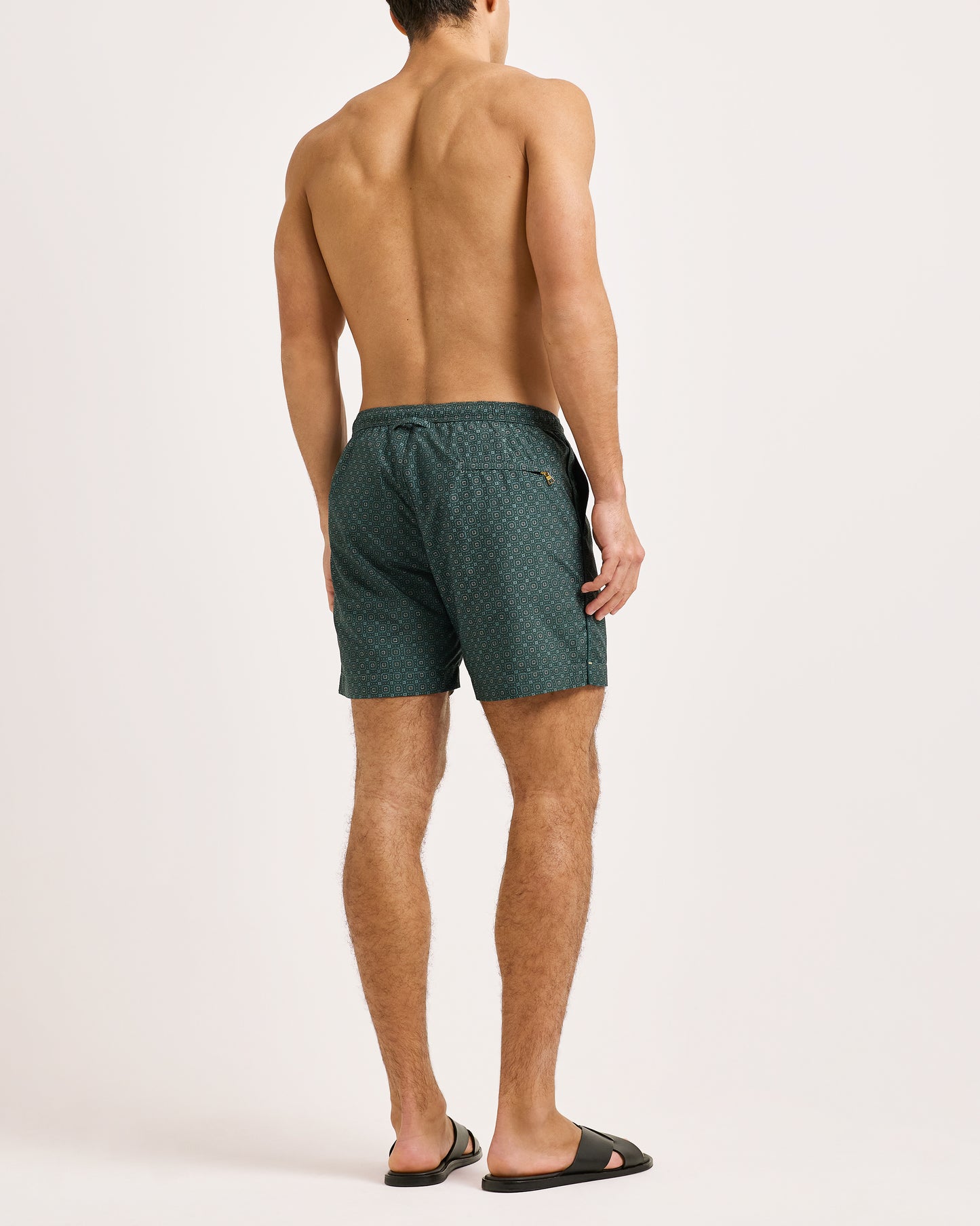 Man wearing green patterned swim shorts on a white background