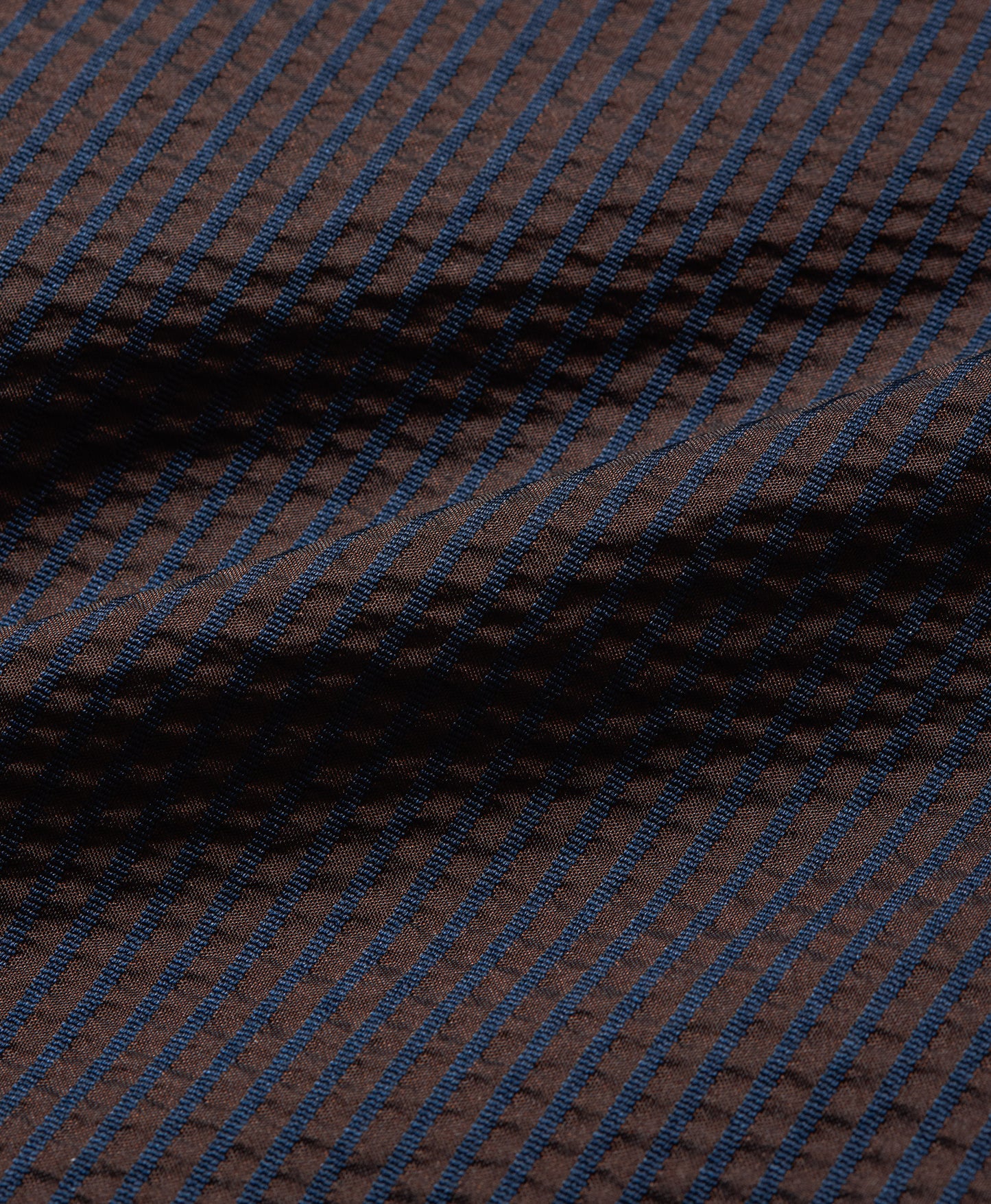 A close-up of a textured fabric with a dark brown base and thin, repeating blue diagonal stripes.