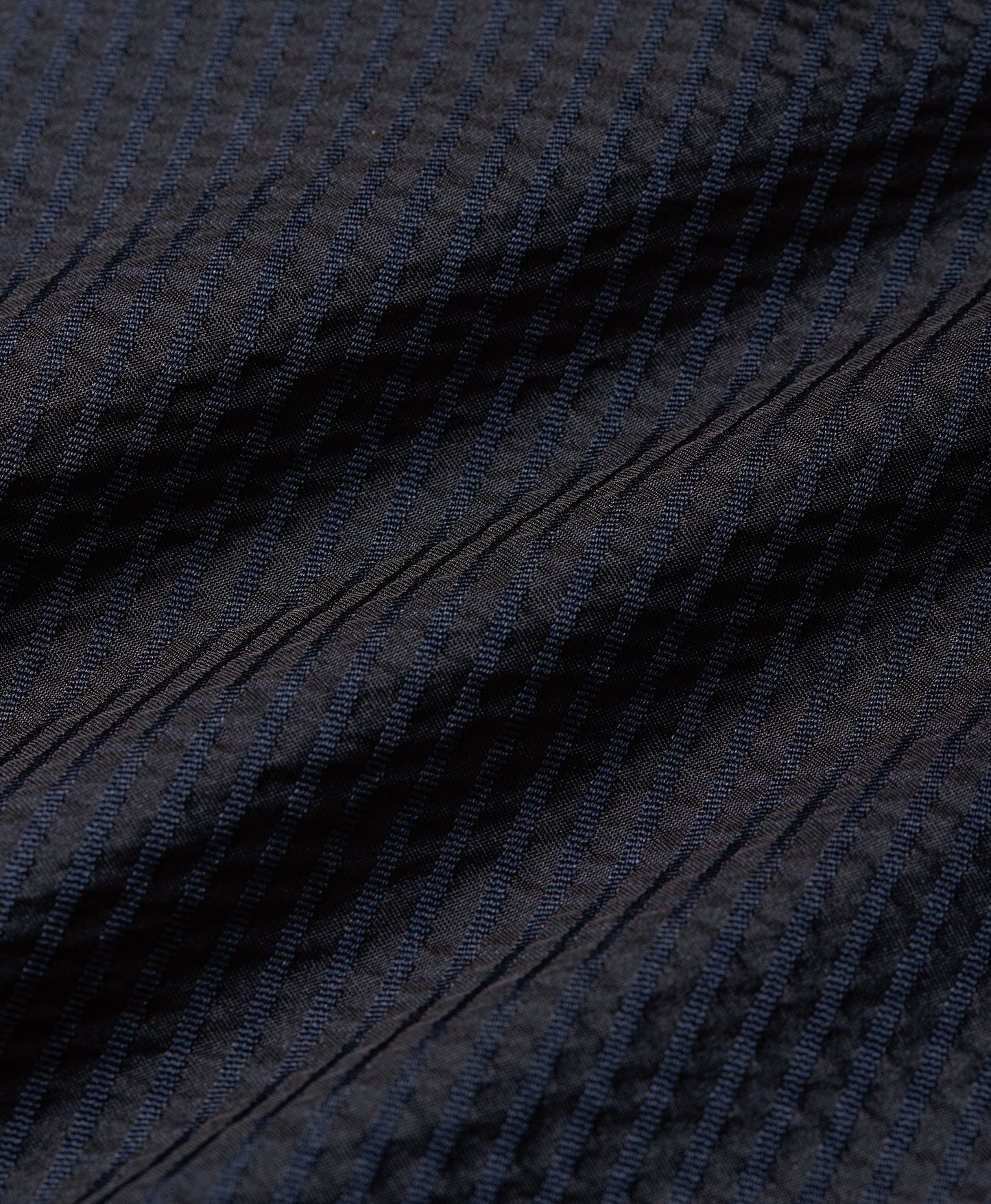 Close-up of a dark navy blue textured fabric with fine vertical ribbing and diagonal stitched details.