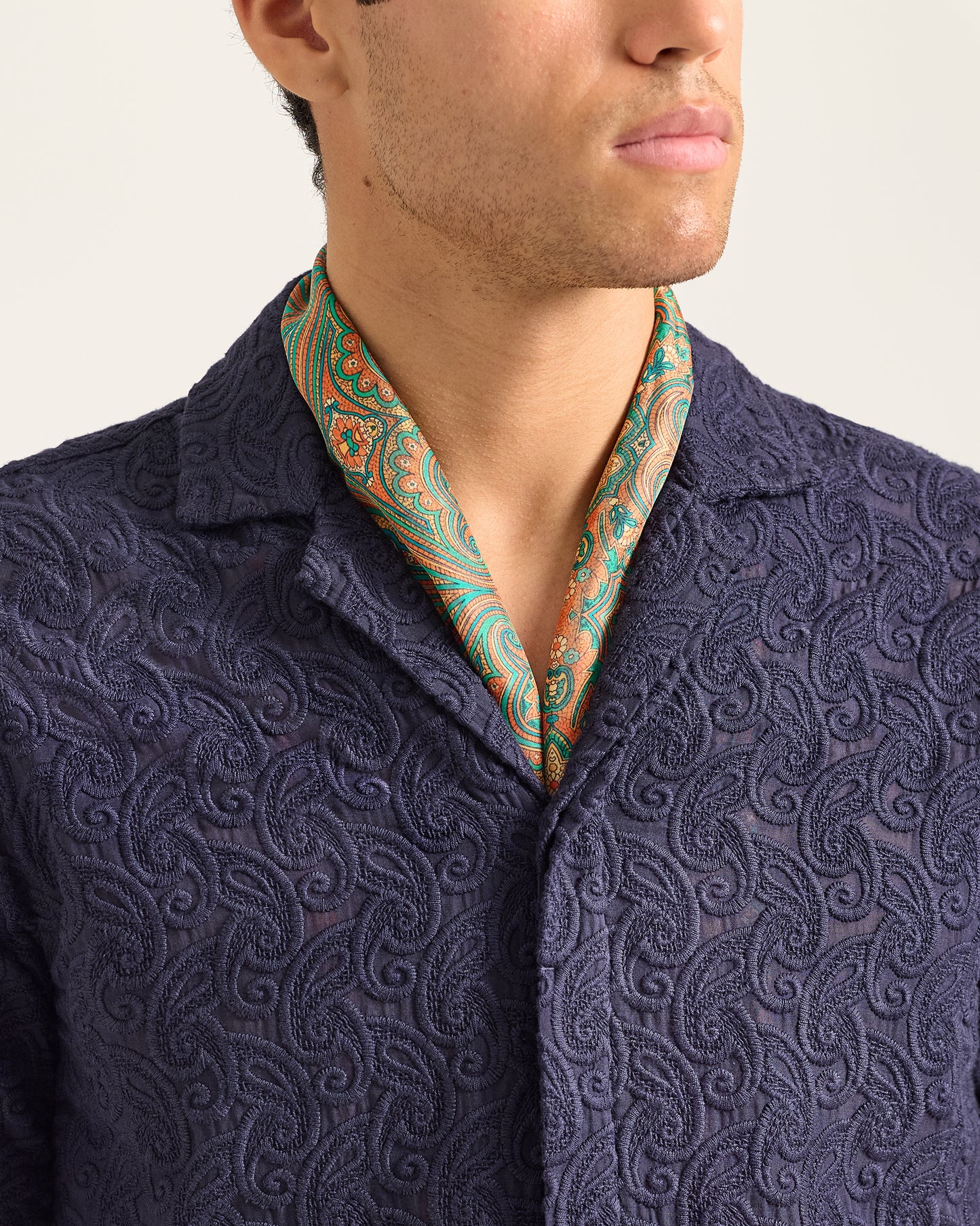 Closeup detail of embroidered navy shirt worn with a neck scarf on a plain background