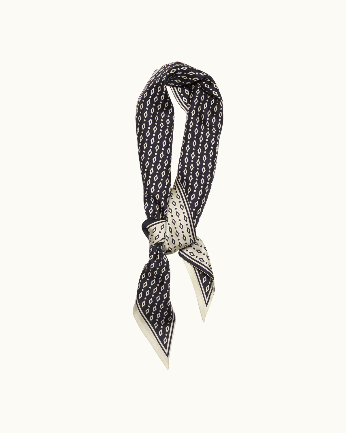 A black silk scarf with a repeating white monogram pattern, tied in a knot to display its double-sided design, set against a solid off-white background.