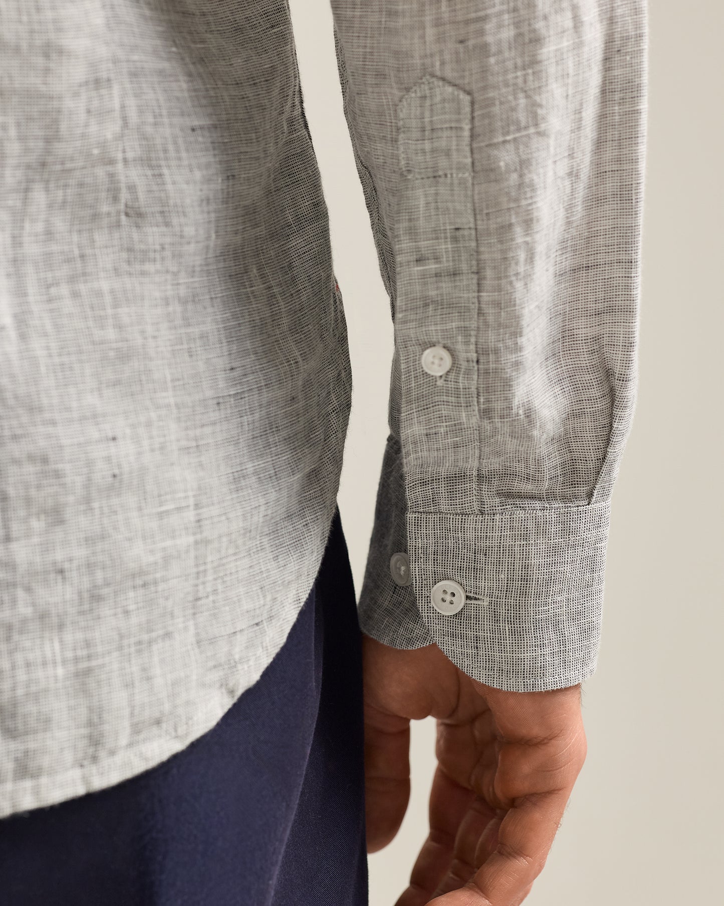 Close-up of a person wearing a gray checkered shirt with rolled-up sleeves on a neutral background