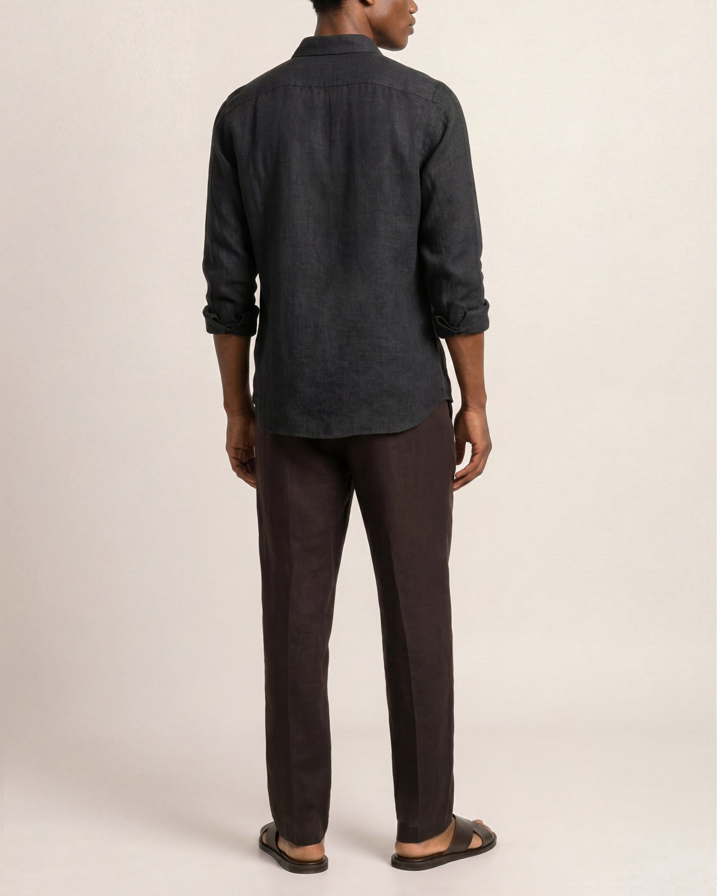 Person wearing a dark denim shirt and brown pants on a beige background