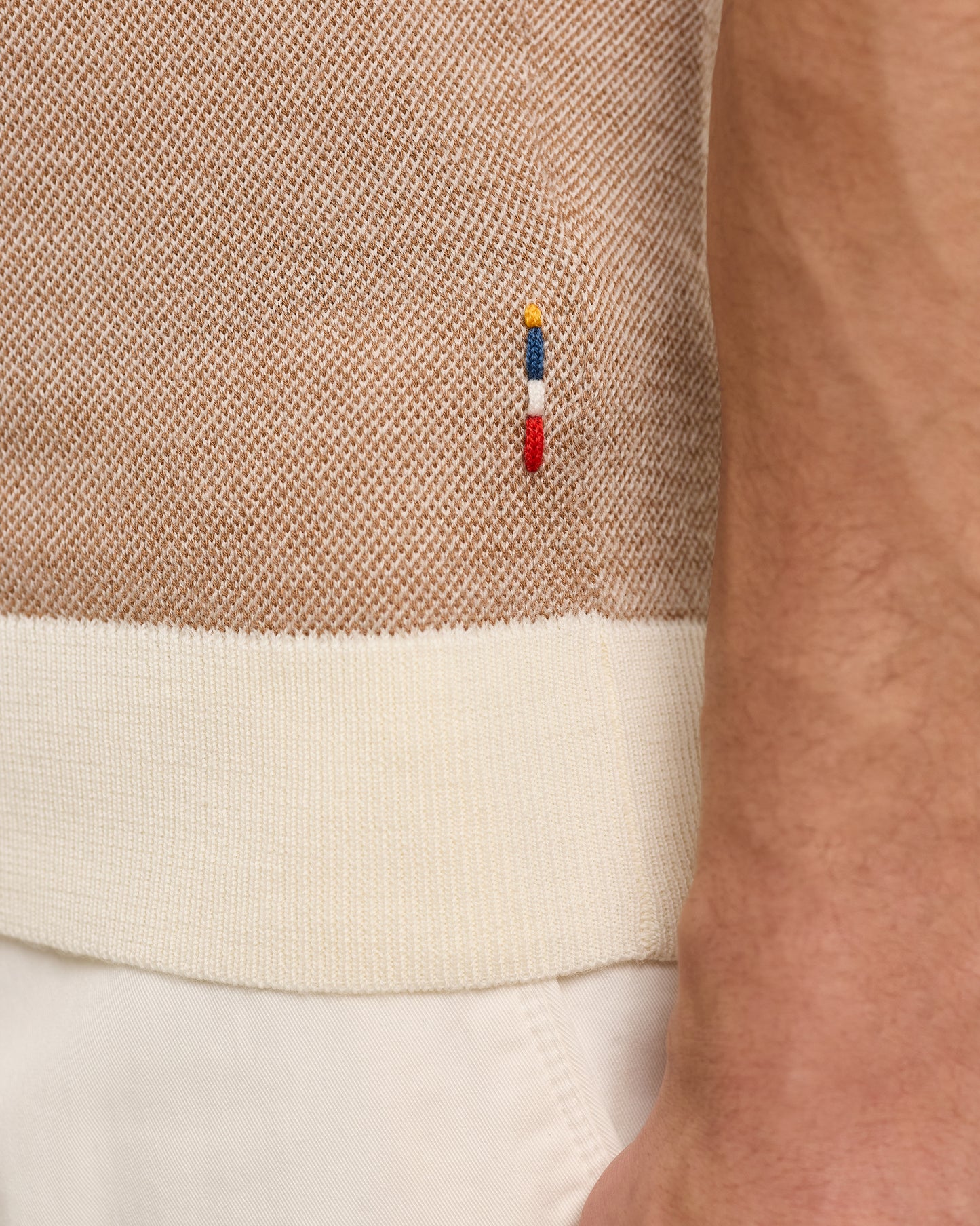 Close-up of a beige sweater with a brand logo on a white background
