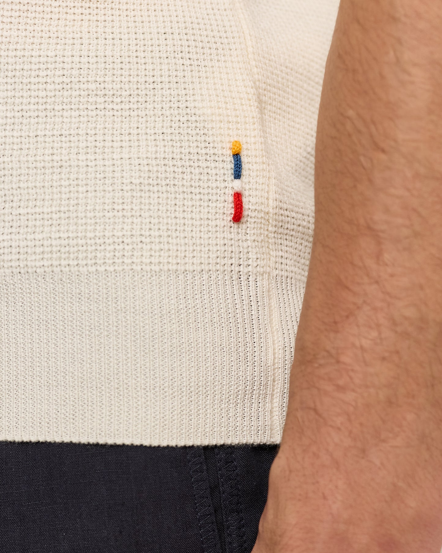 Close-up of a textured beige sweater with colorful embroidered details on a person wearing it.