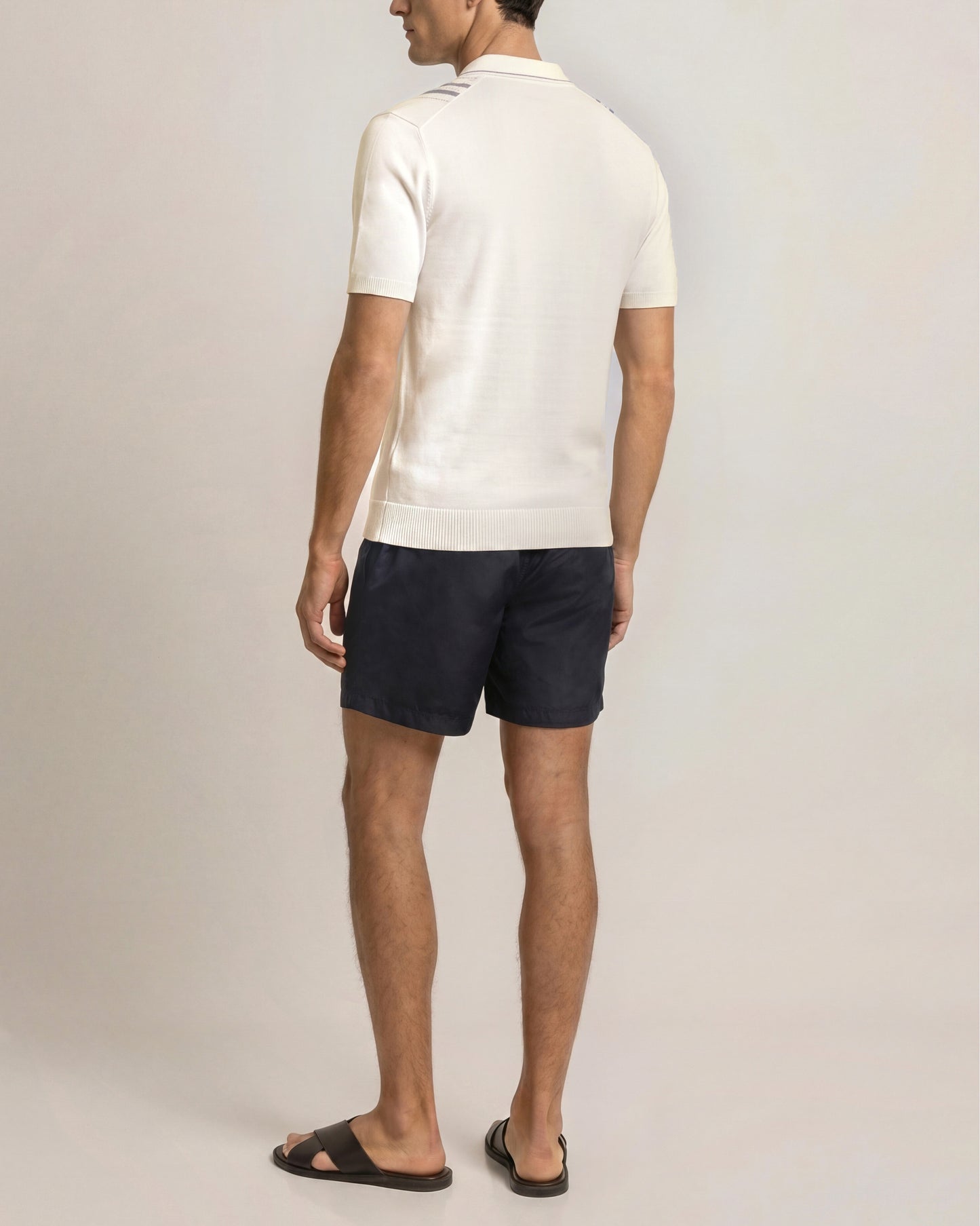 Man wearing a white polo shirt and navy shorts on a plain background