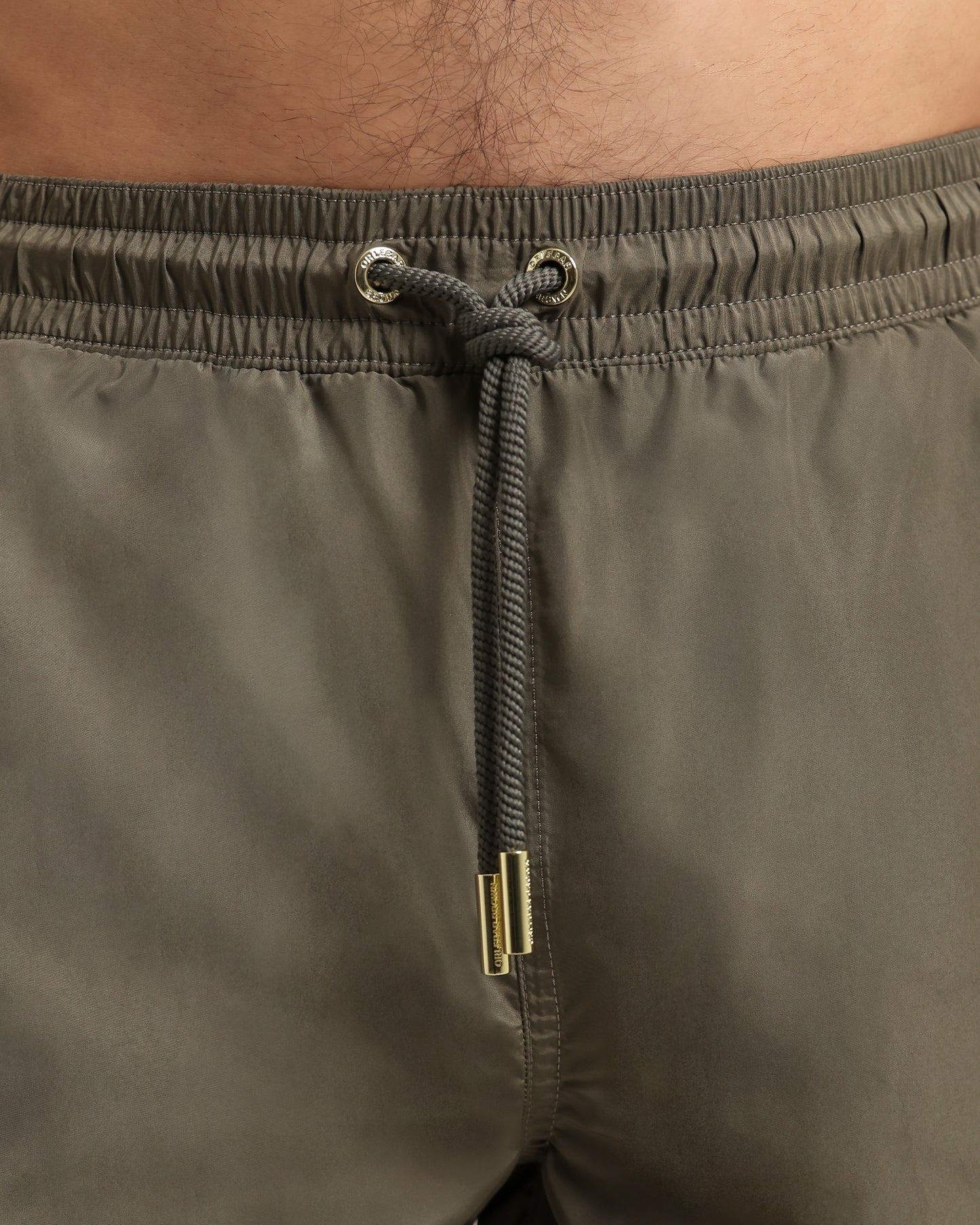 Close-up of olive green swim shorts with drawstring and metal buckle.