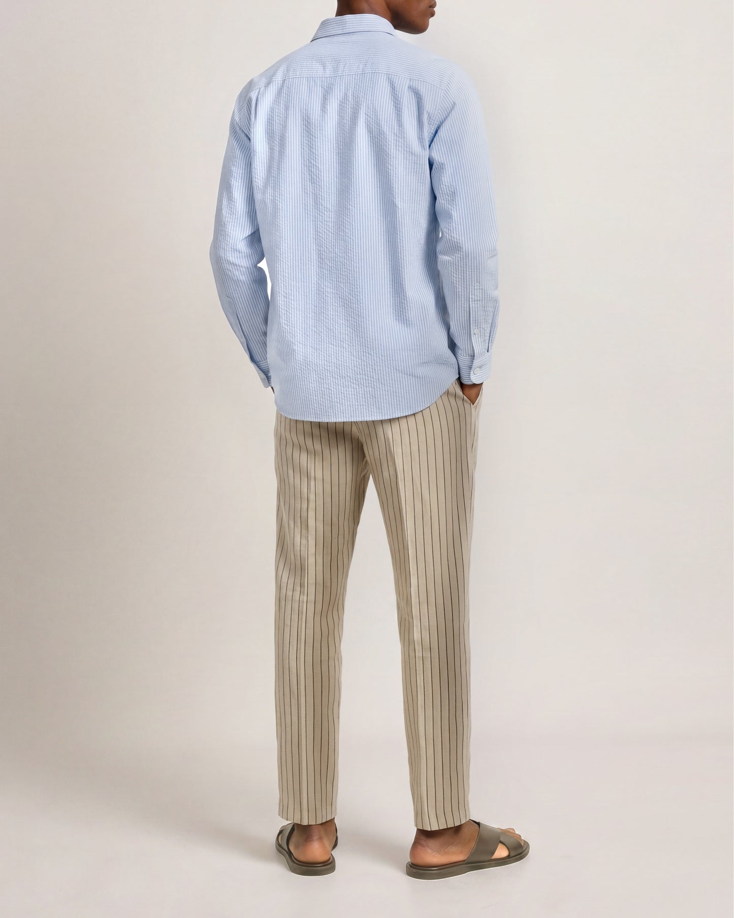 Person wearing a light blue shirt and beige striped pants on a plain background