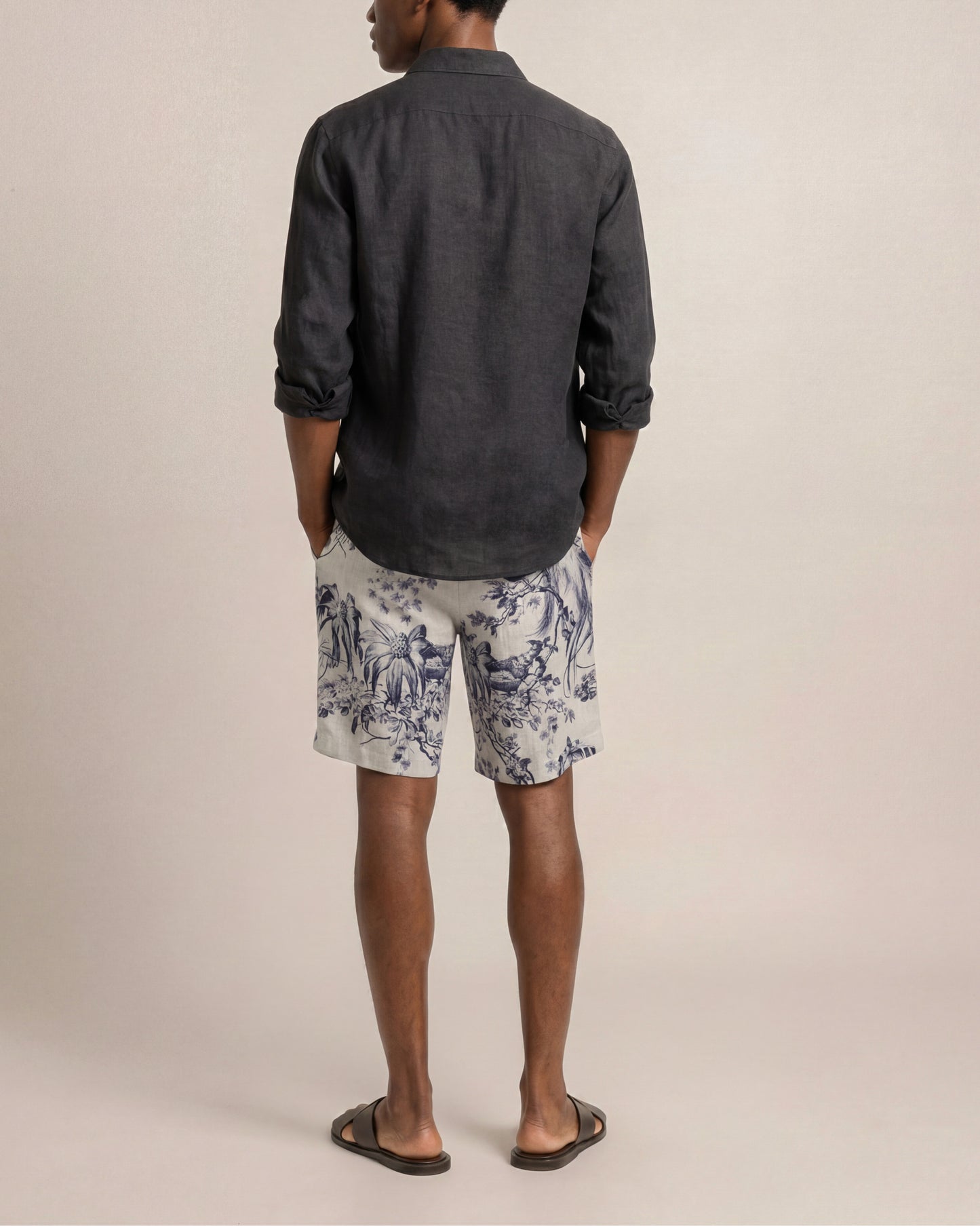 Person wearing a dark shirt and patterned shorts on a plain background