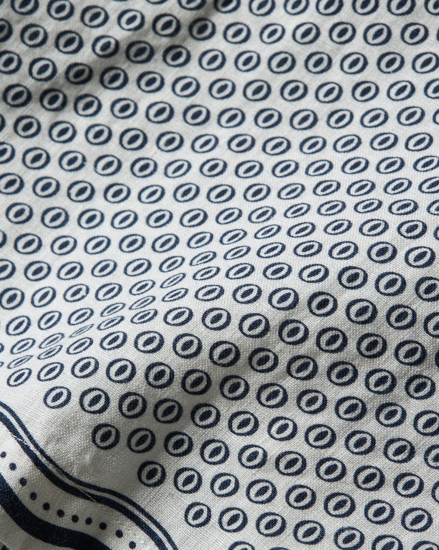 Close-up of a white fabric with a repeating navy blue circular dot pattern and a navy border along the bottom edge.