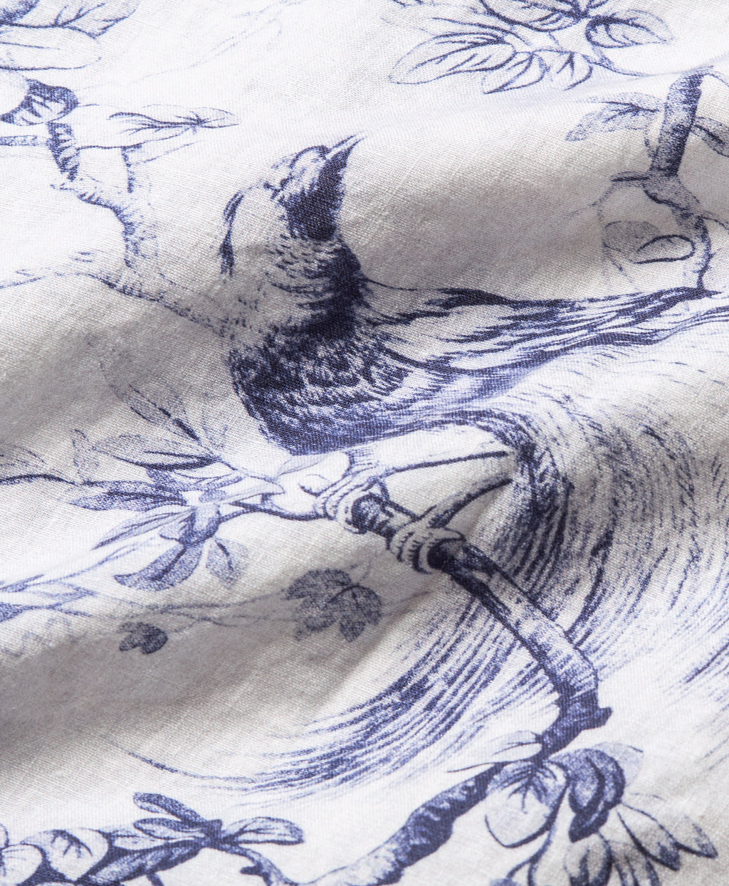 A close-up of a white fabric with a blue toile-style print of a bird perched on branches.
