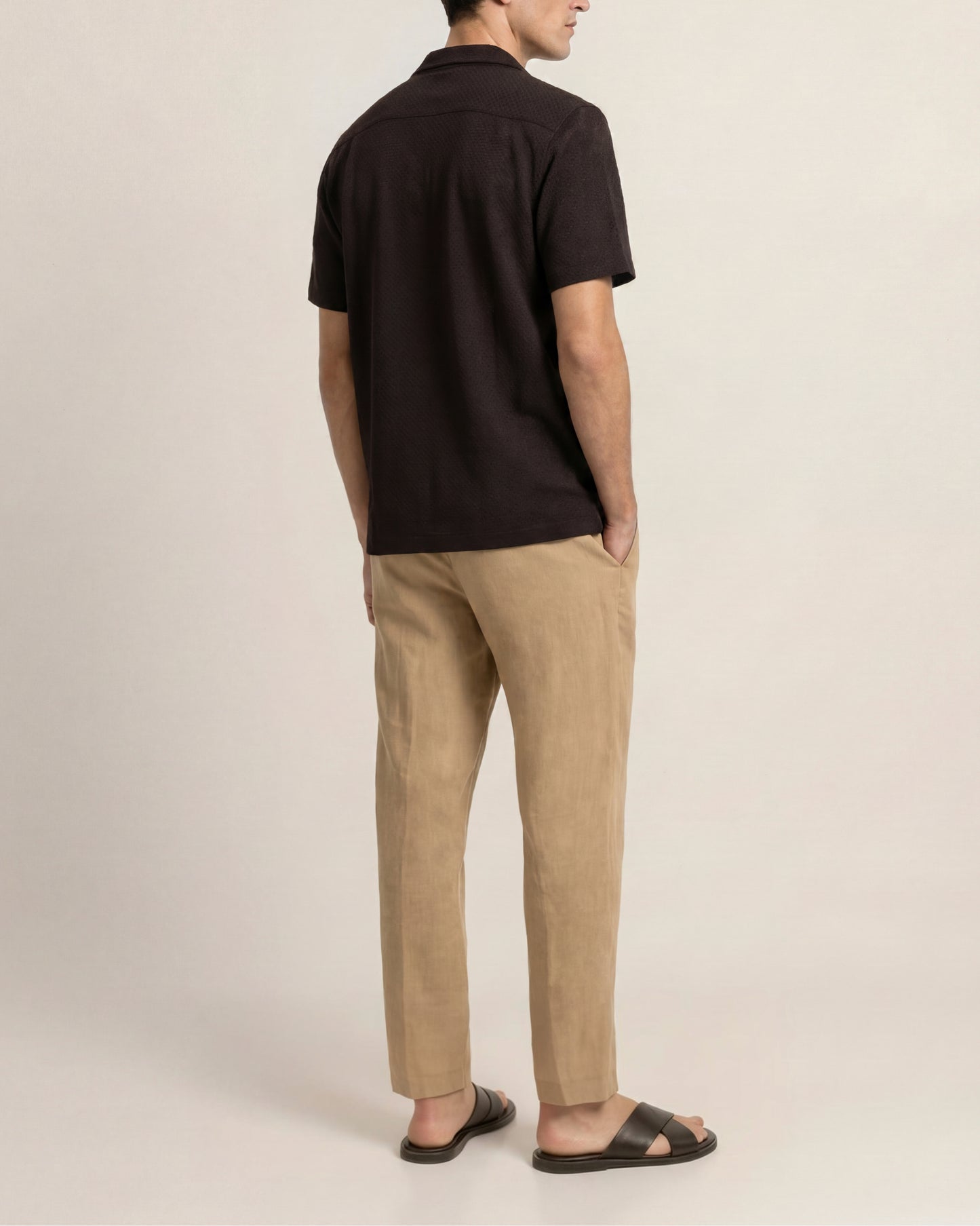 Person wearing a black polo shirt and beige pants on a plain background