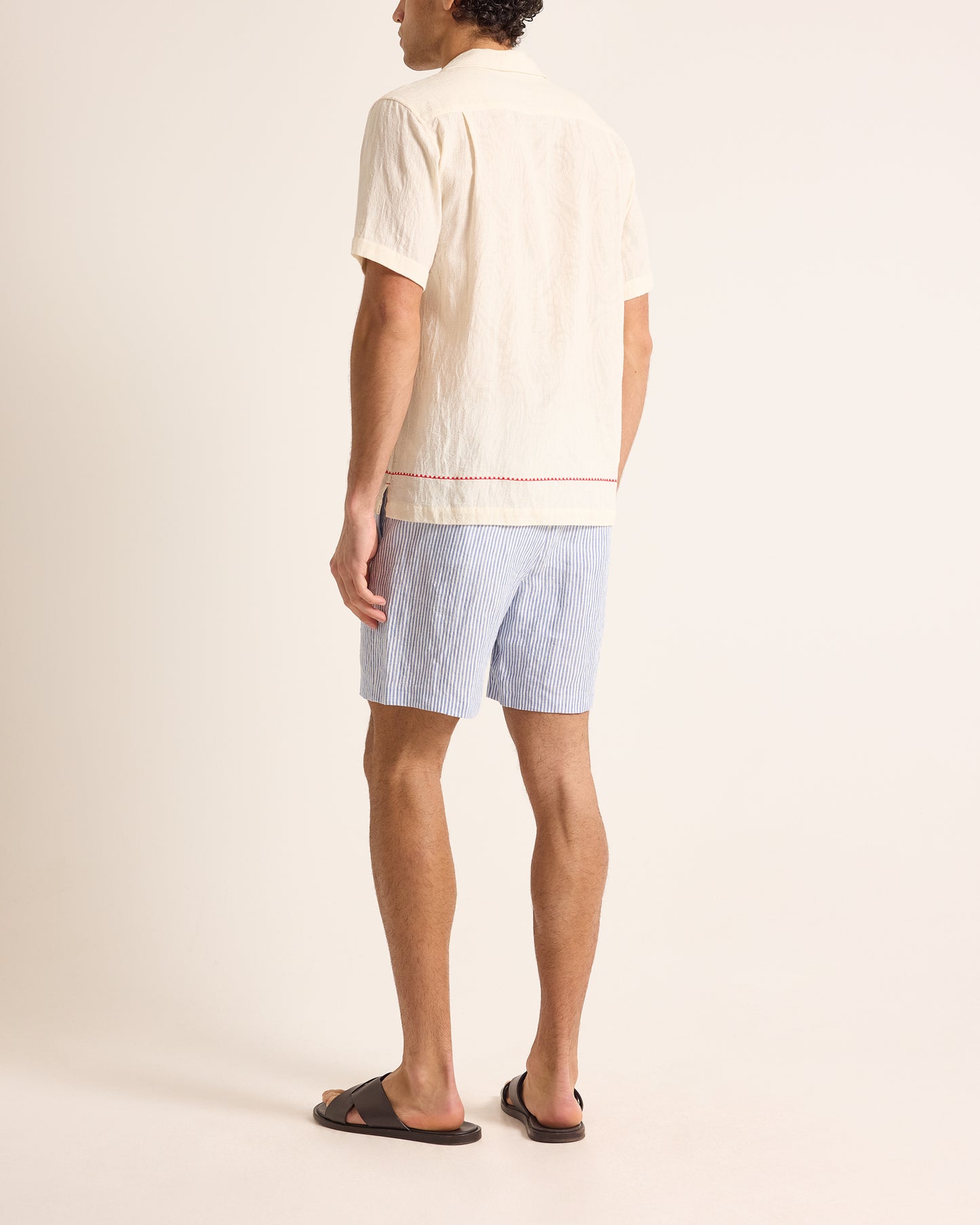 Person wearing a light-colored shirt and blue shorts on a plain background