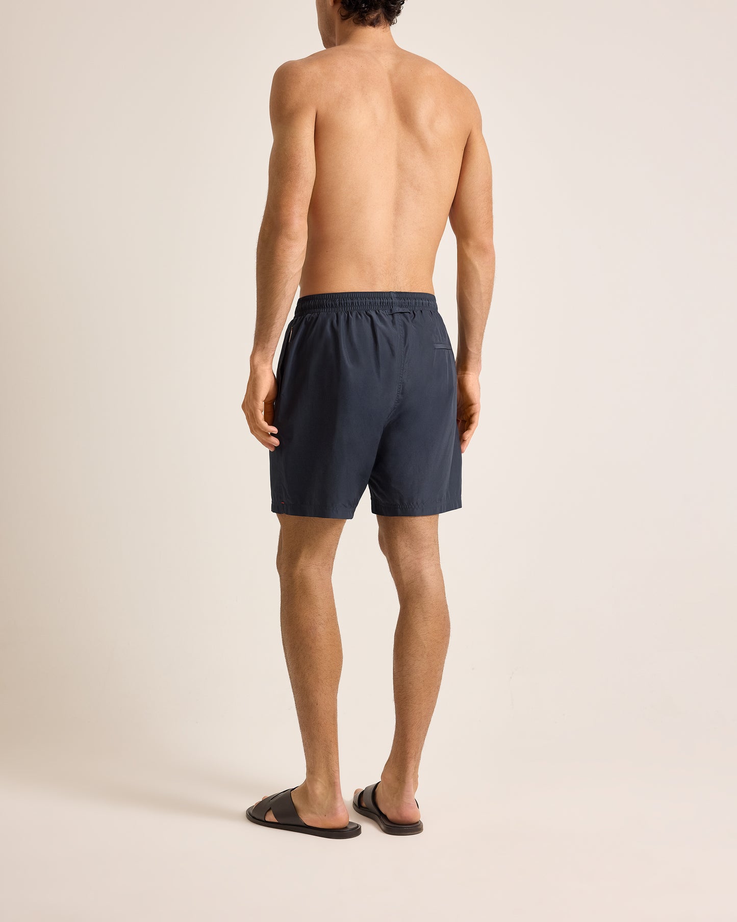 Man wearing navy blue swim shorts on a beige background