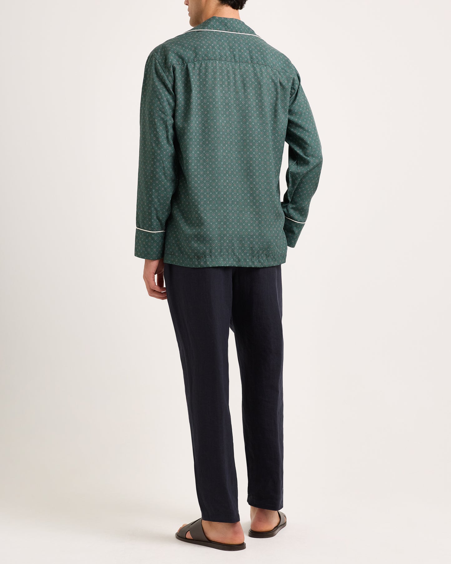 Person wearing a green patterned jacket and dark pants on a white background