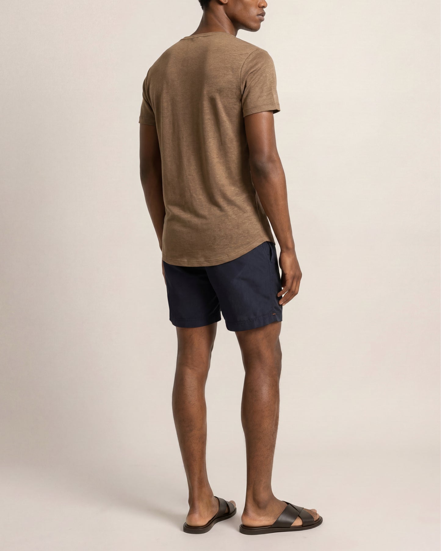 Man wearing a brown t-shirt and navy shorts on a beige background