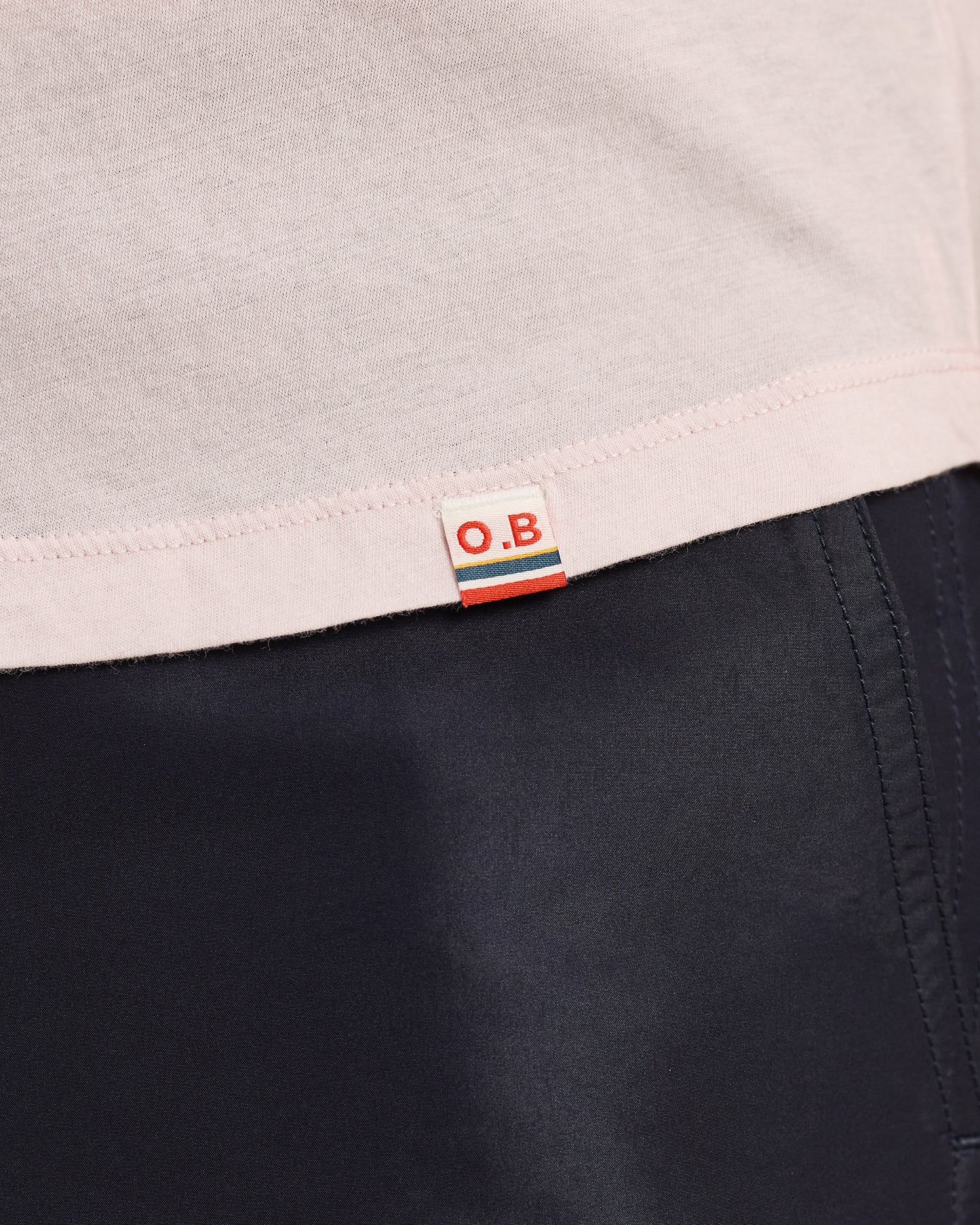 Close-up of a label with 'O.B.' on a garment with a light gray top and dark fabric.