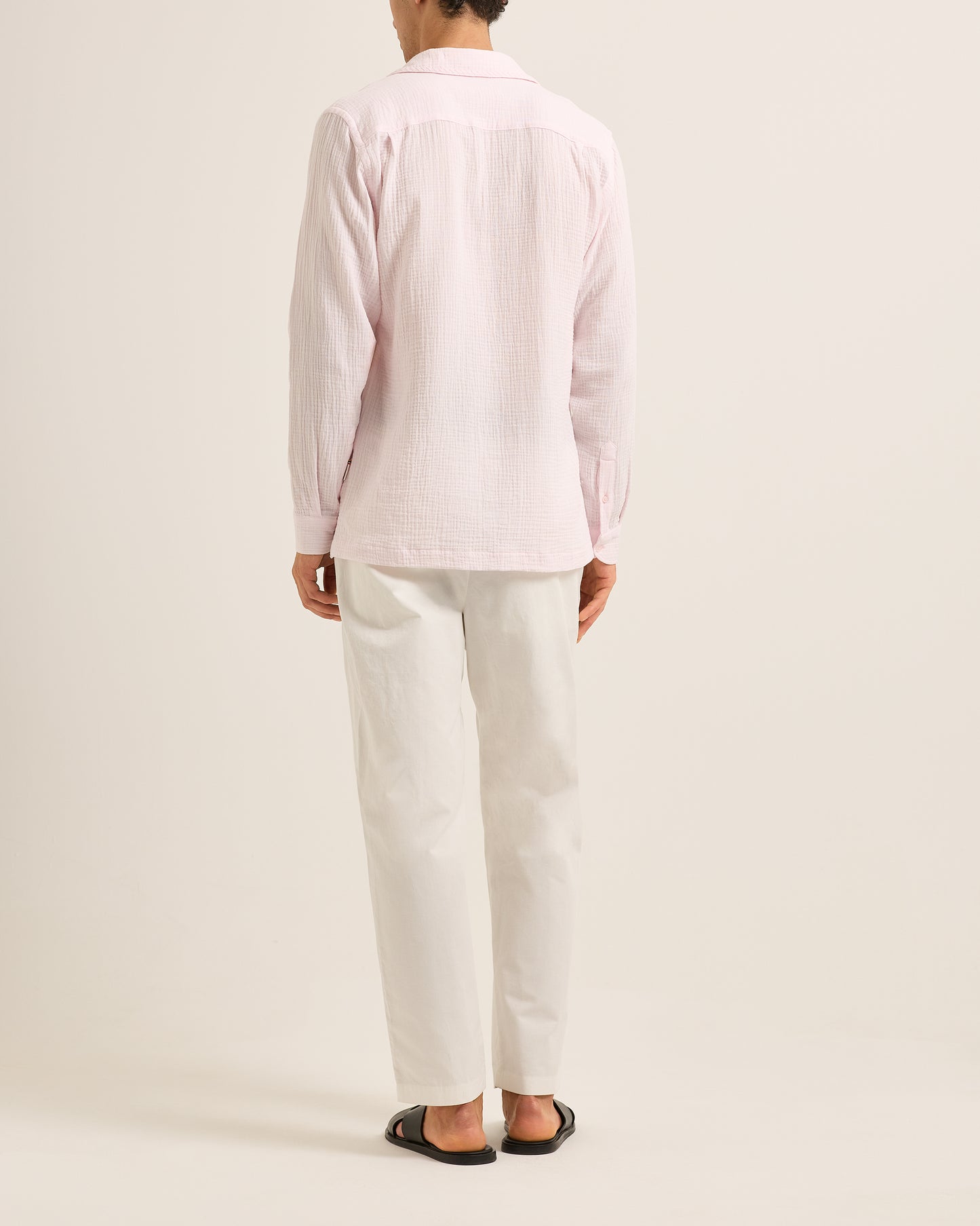 Person wearing a light pink shirt and white pants on a plain background