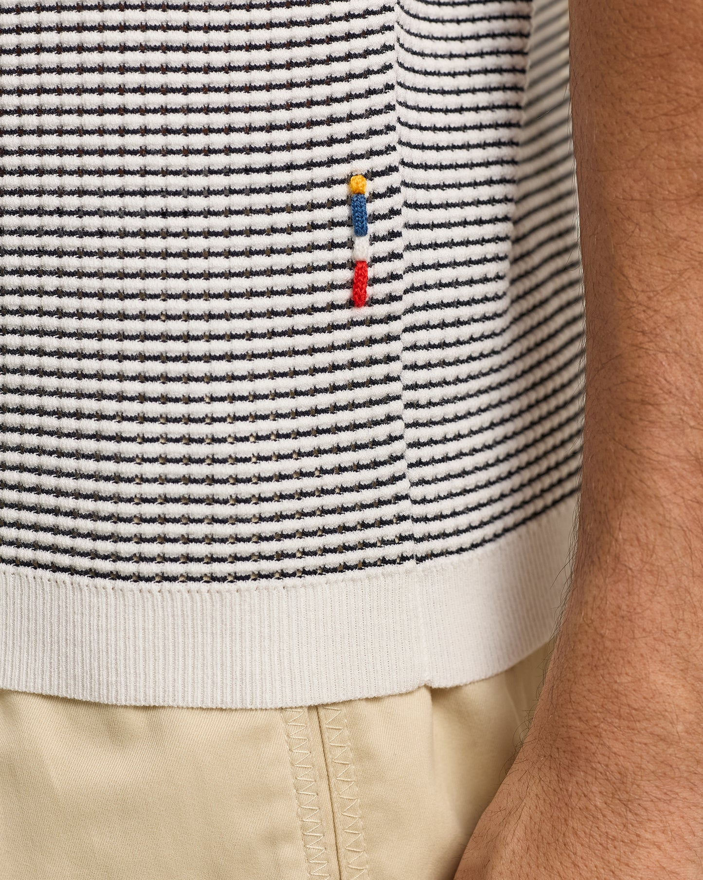 Close-up of a striped polo with a small logo on a person wearing beige pants.