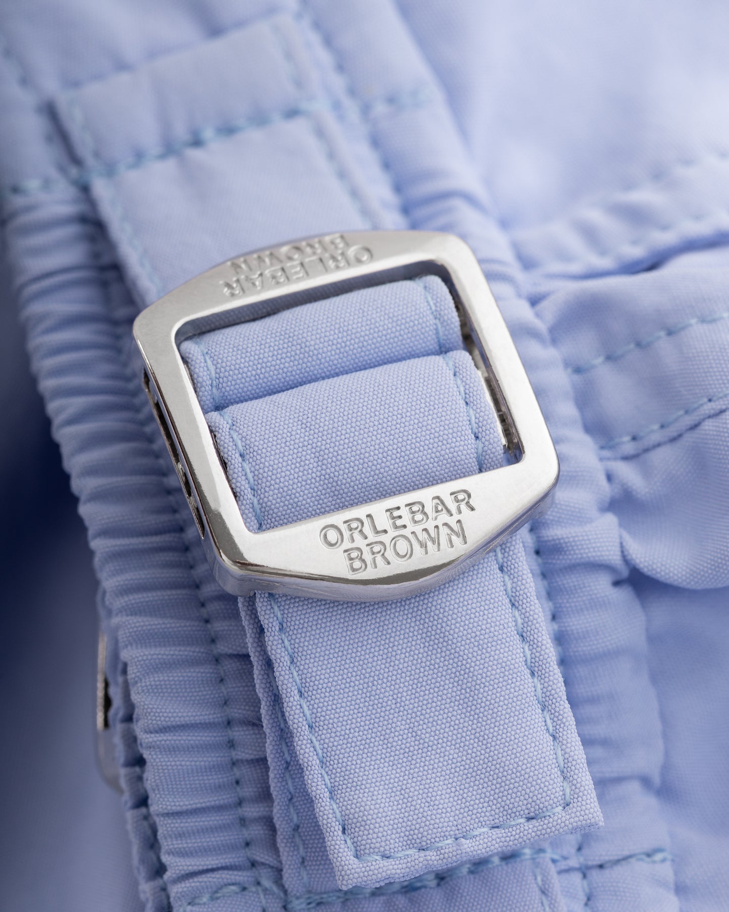 Close-up of a blue garment with a silver buckle and 'Orlebar Brown' branding.