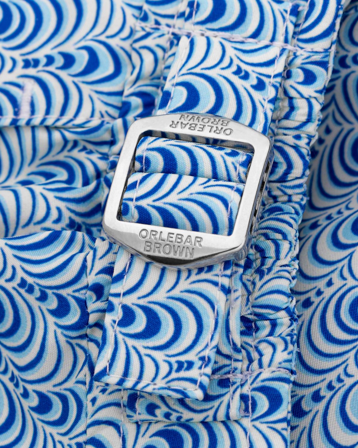 Close-up of a blue and white patterned fabric strap with a silver metal buckle engraved with the brand name ORLEBAR BROWN.
