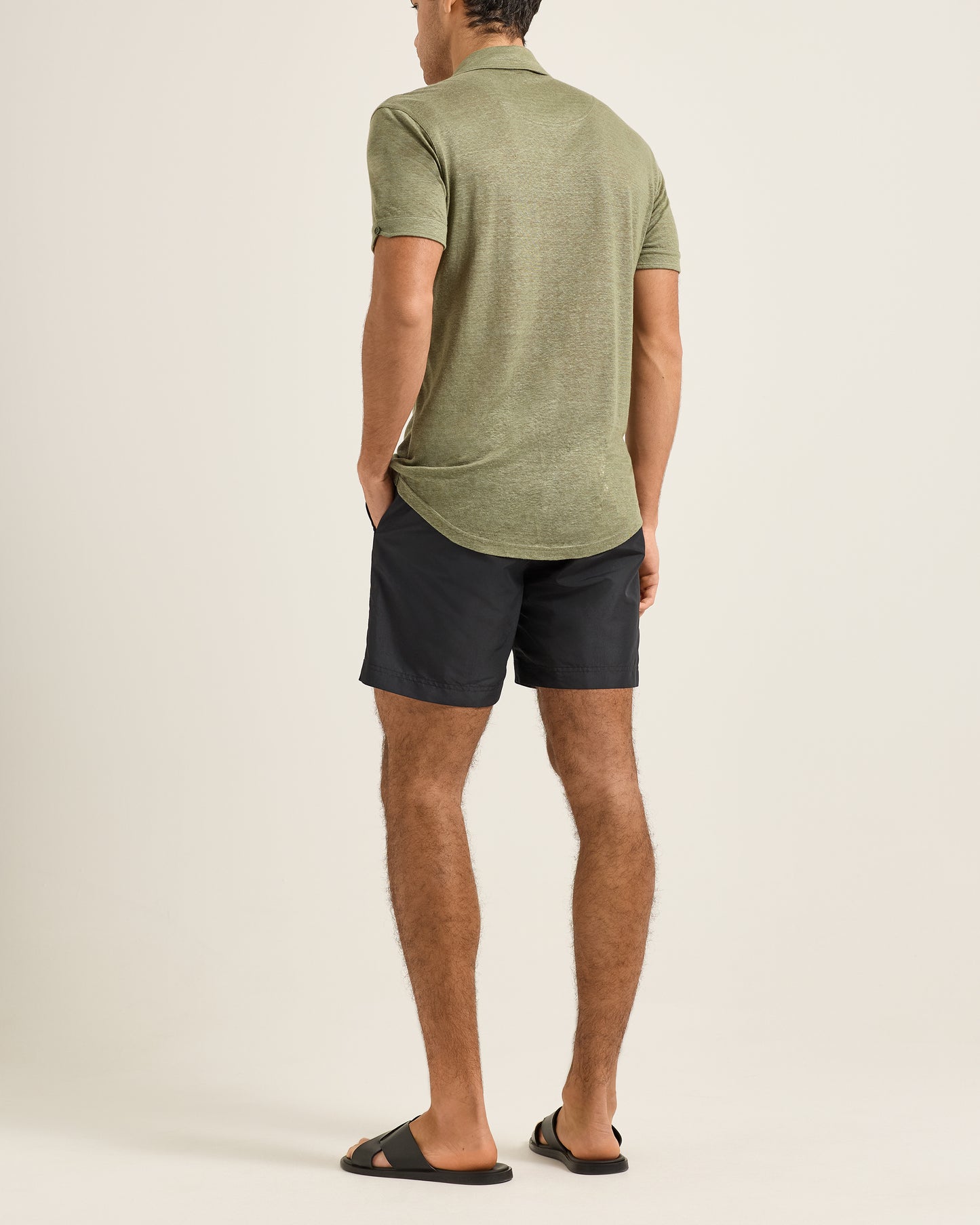 Man wearing a green polo shirt and black shorts on a beige background
