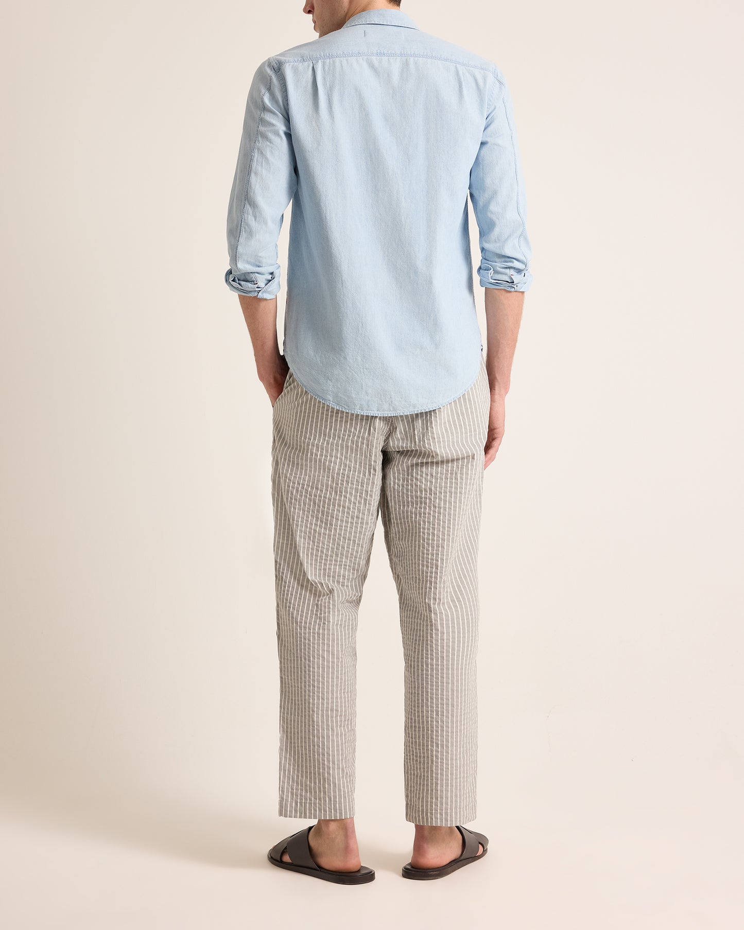 Man wearing light grey trousers with light stripe and drawstring waist, worn with a light blue shirt on a plain background
