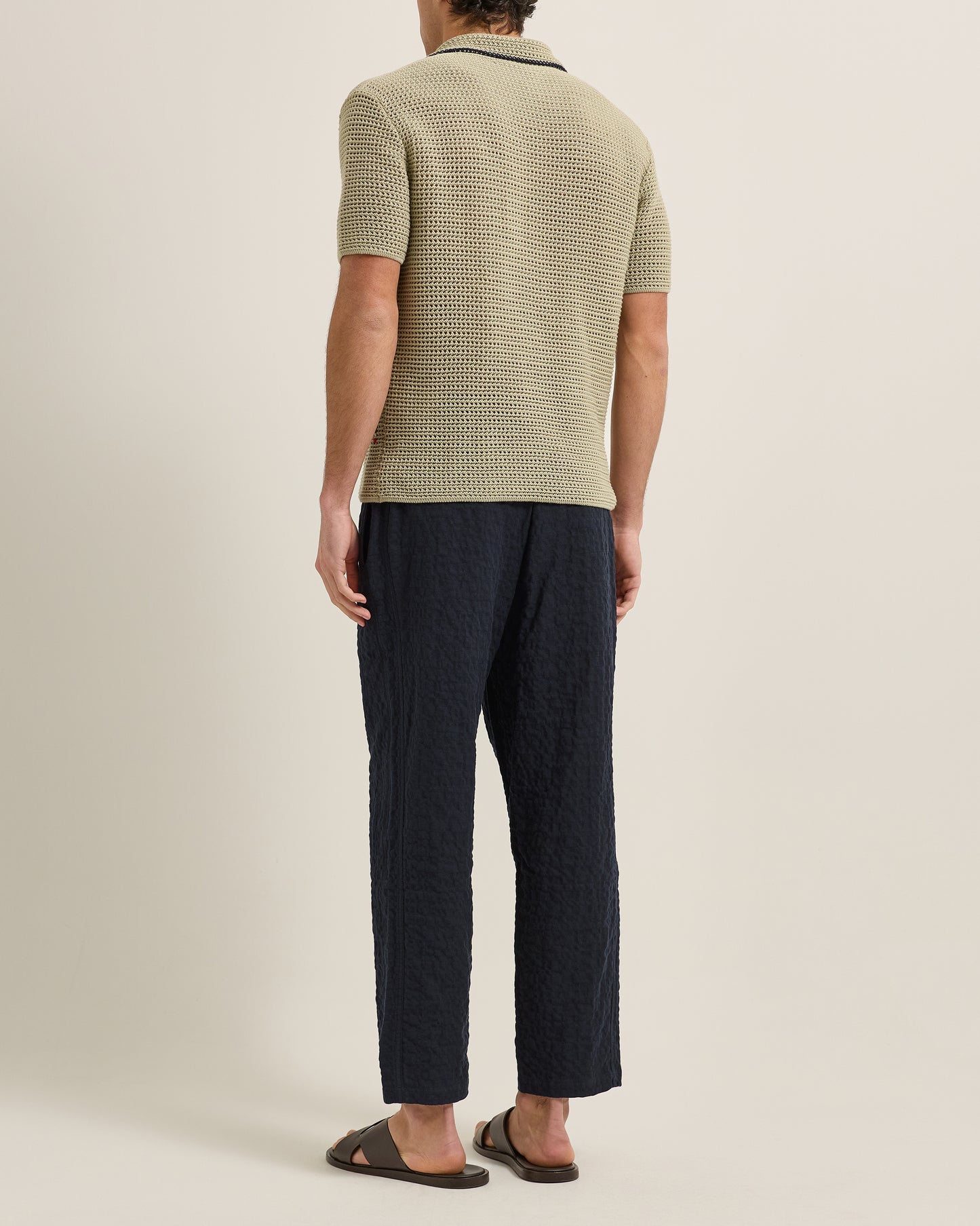 Person wearing a textured green shirt and dark pants on a plain background