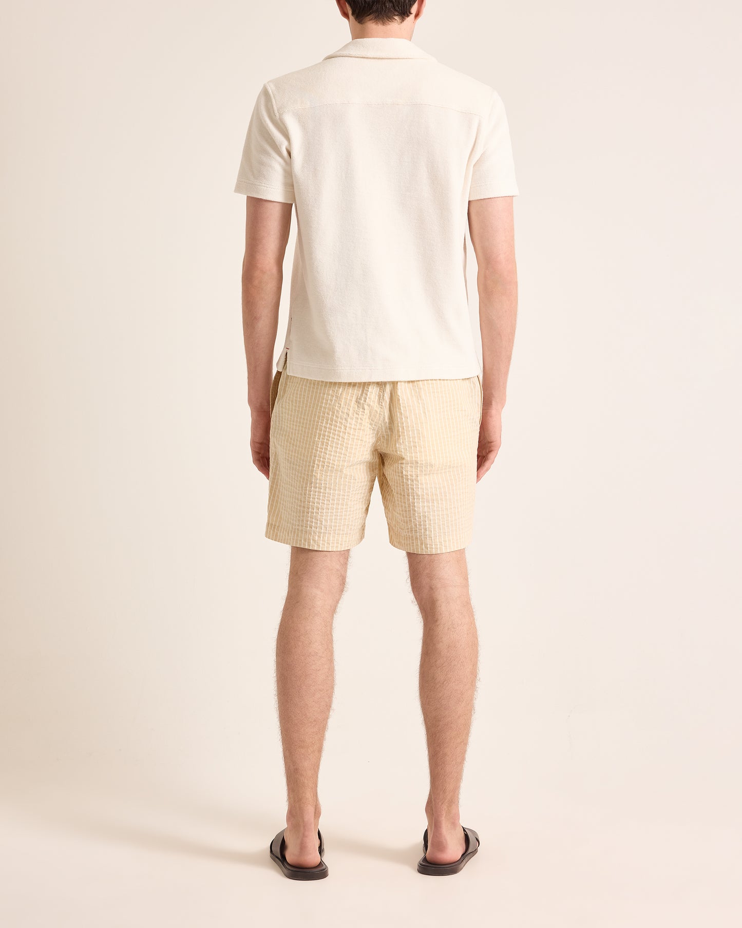Person wearing a white polo shirt and striped checkered shorts on a beige background