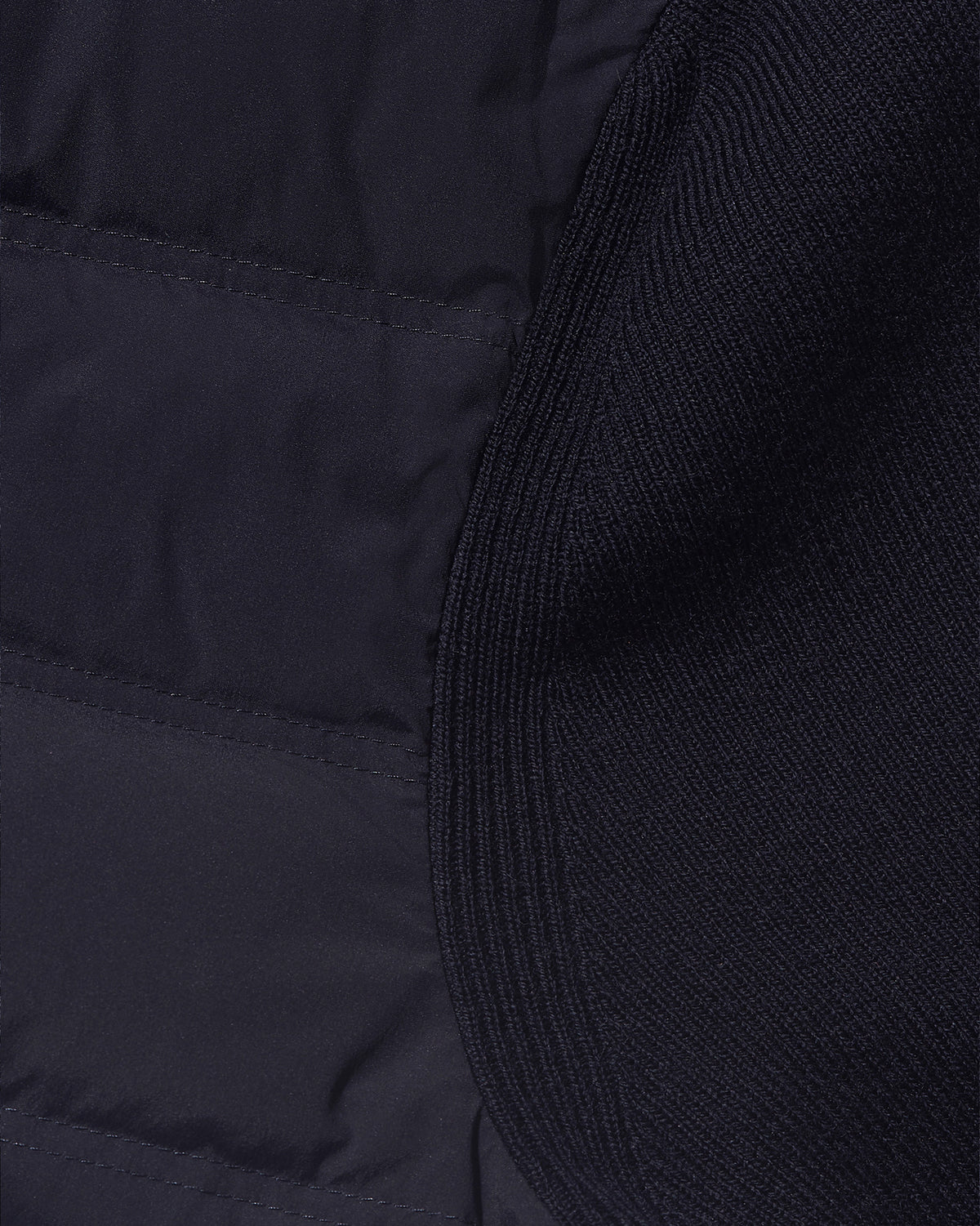 Close-up detail of a dark navy quilted puffer jacket showing the contrast between smooth padded fabric and ribbed knit trim.