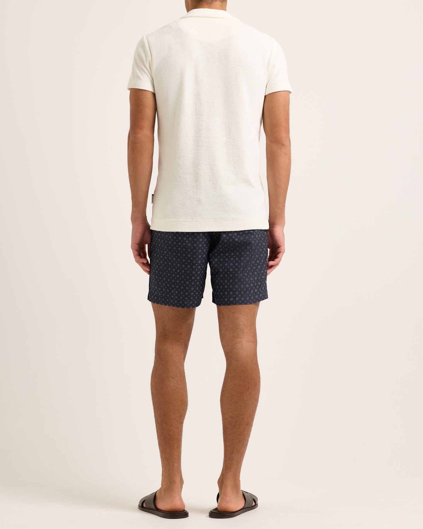 Person wearing a white towelling polo shirt and navy patterned shorts on a plain background