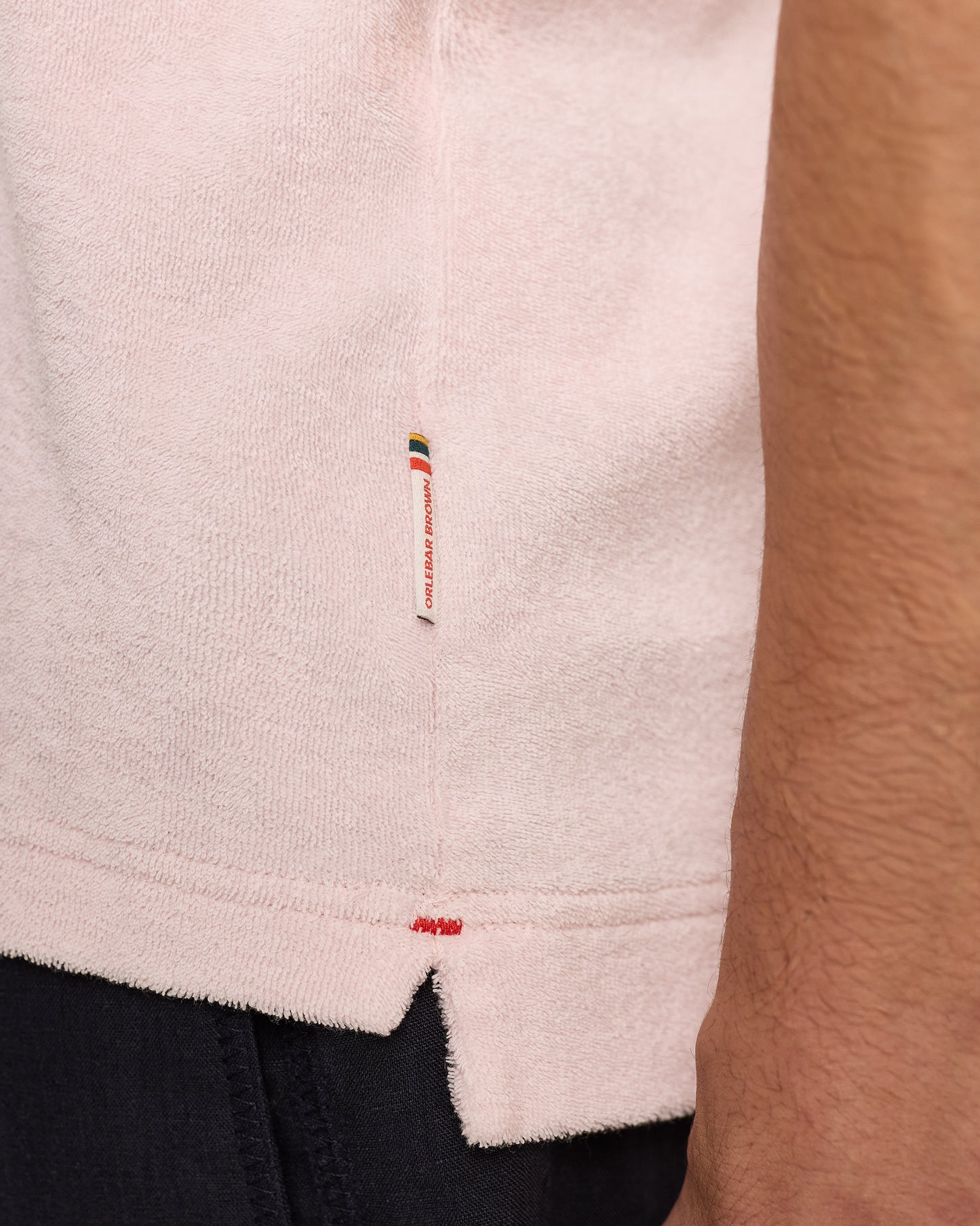 Close-up of a light pink terry towelling with a brand label on a person wearing dark pants.