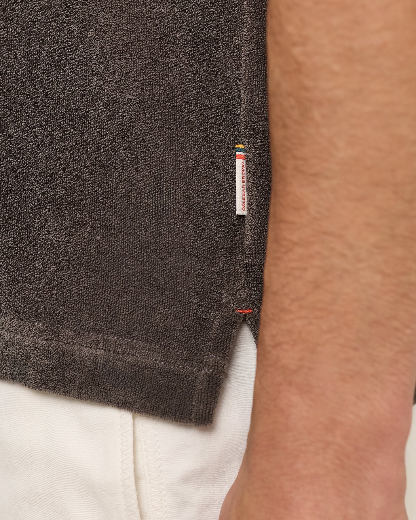 Close-up of a dark gray t-shirt with a brand label on a person wearing white pants.