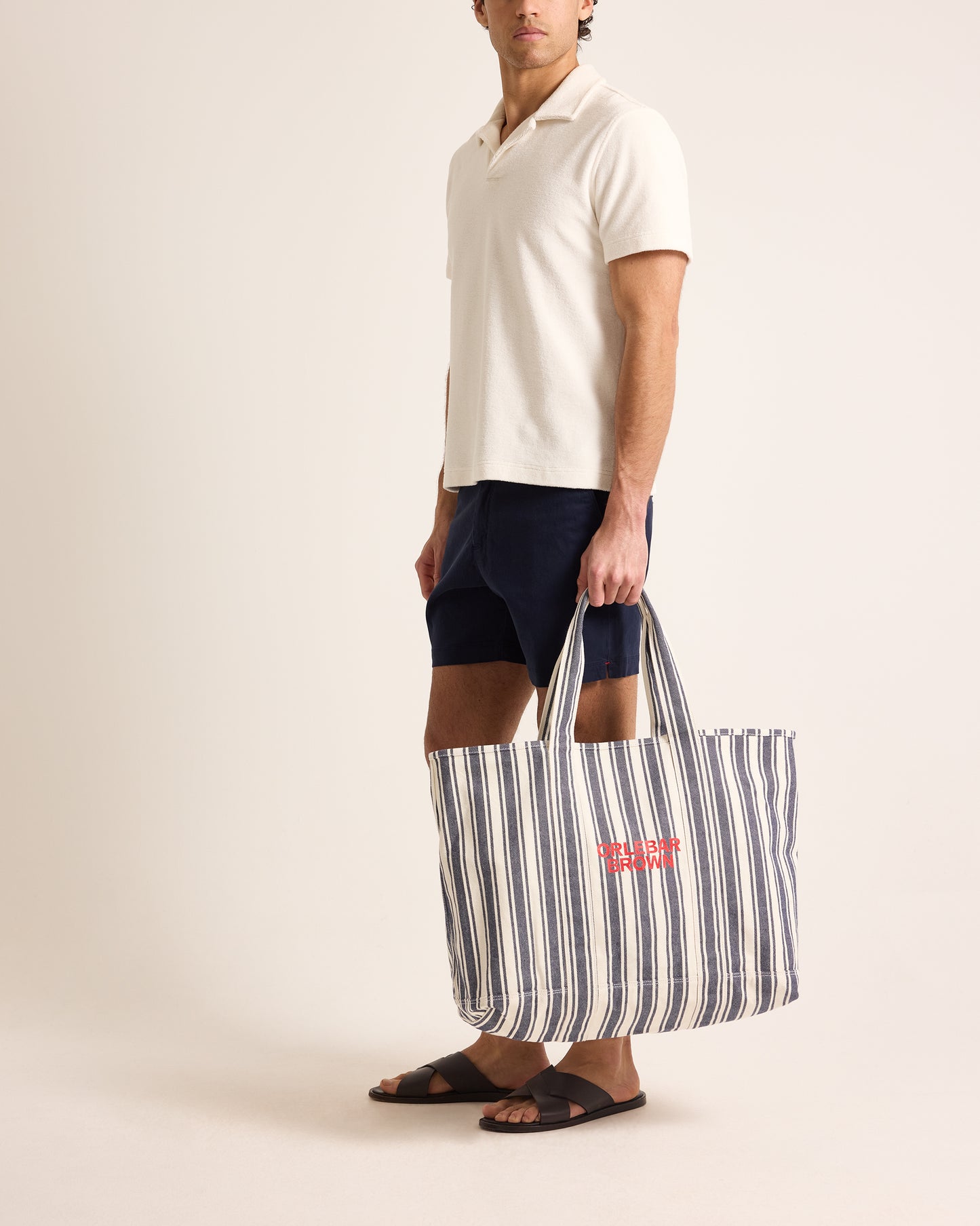Person holding a striped tote bag with a visible brand logo on a plain background
