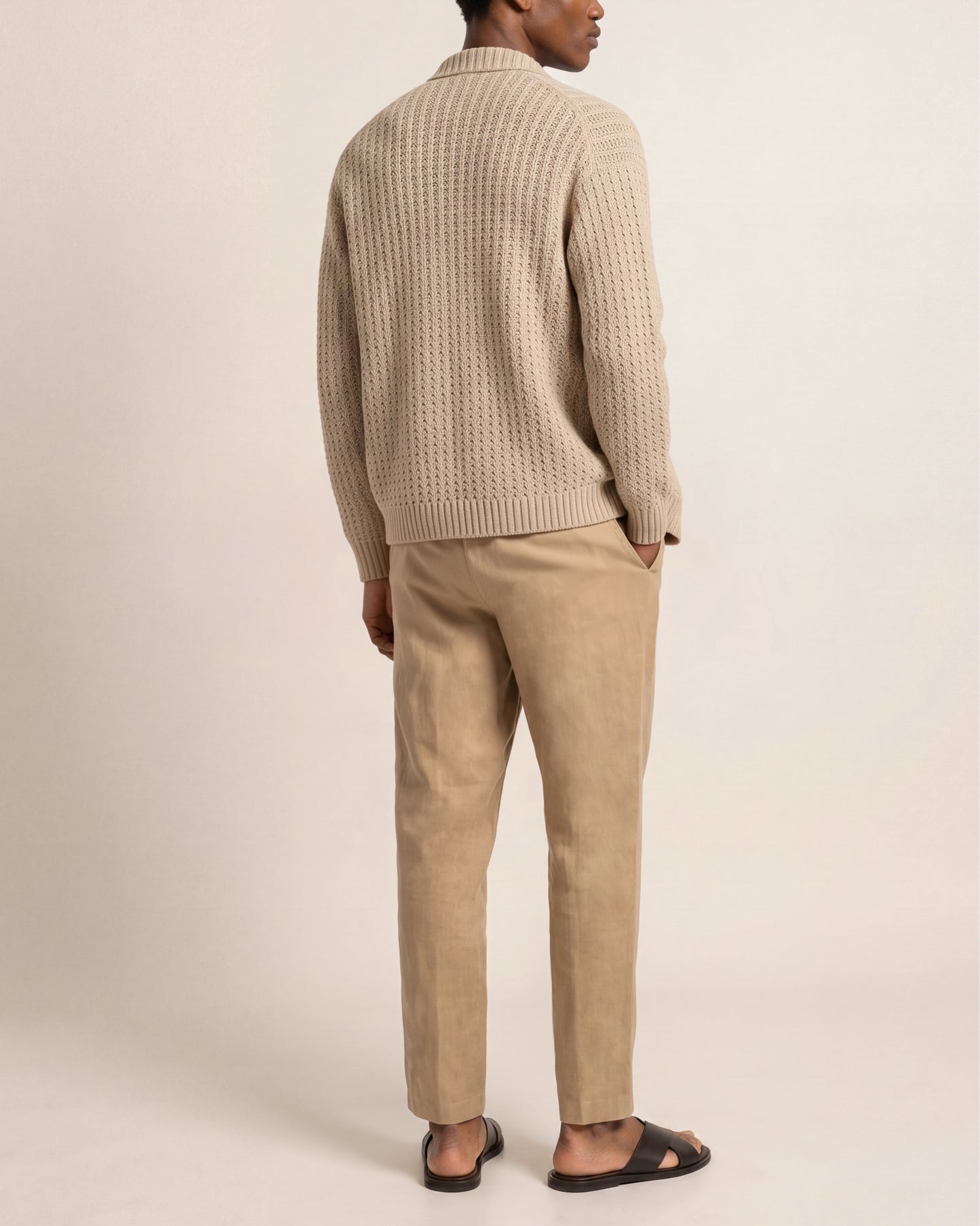Person wearing a beige knitted sweater and matching pants on a plain background